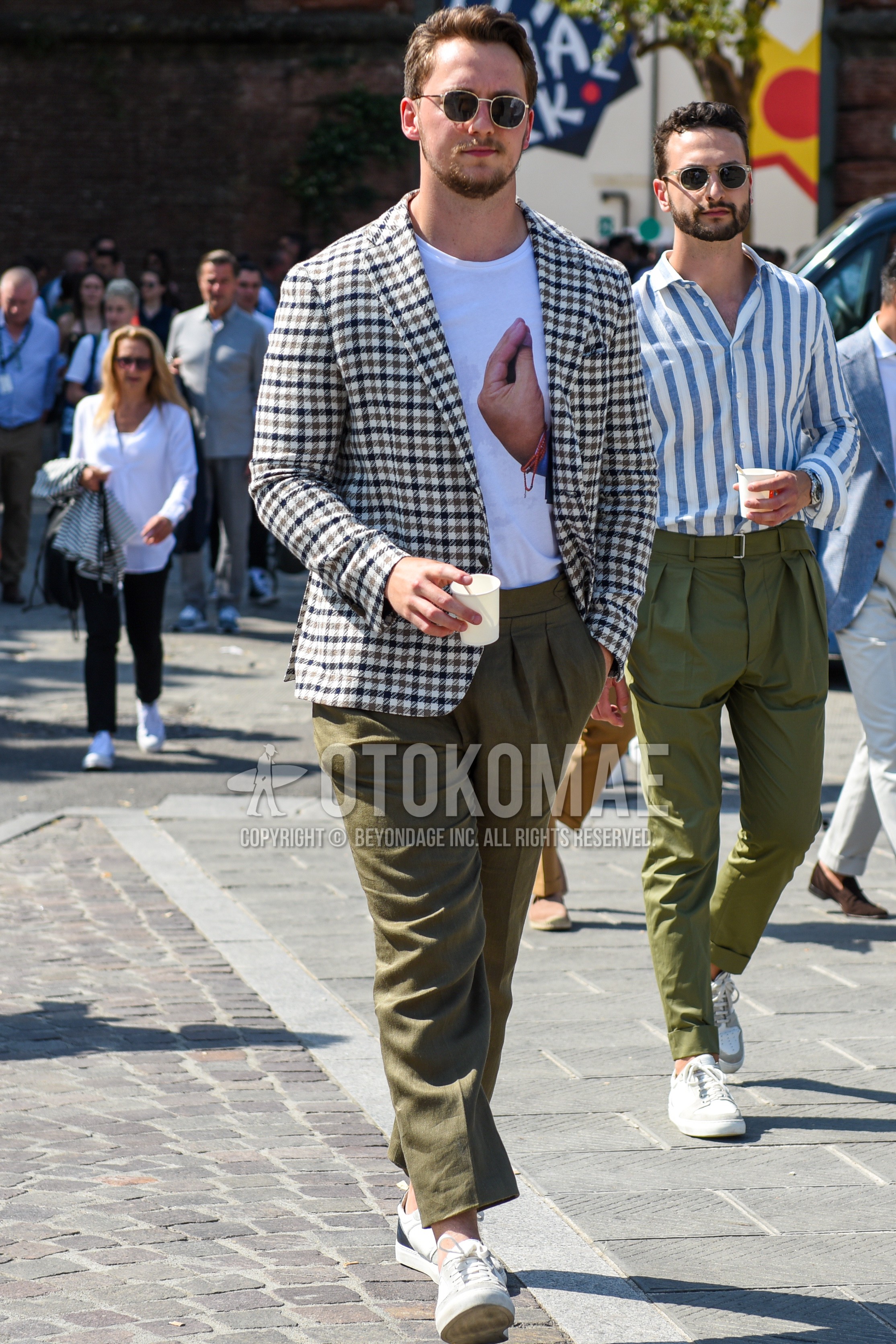 Men's spring summer autumn outfit with silver black plain sunglasses, white brown check tailored jacket, white graphic t-shirt, olive green plain beltless pants, white low-cut sneakers.