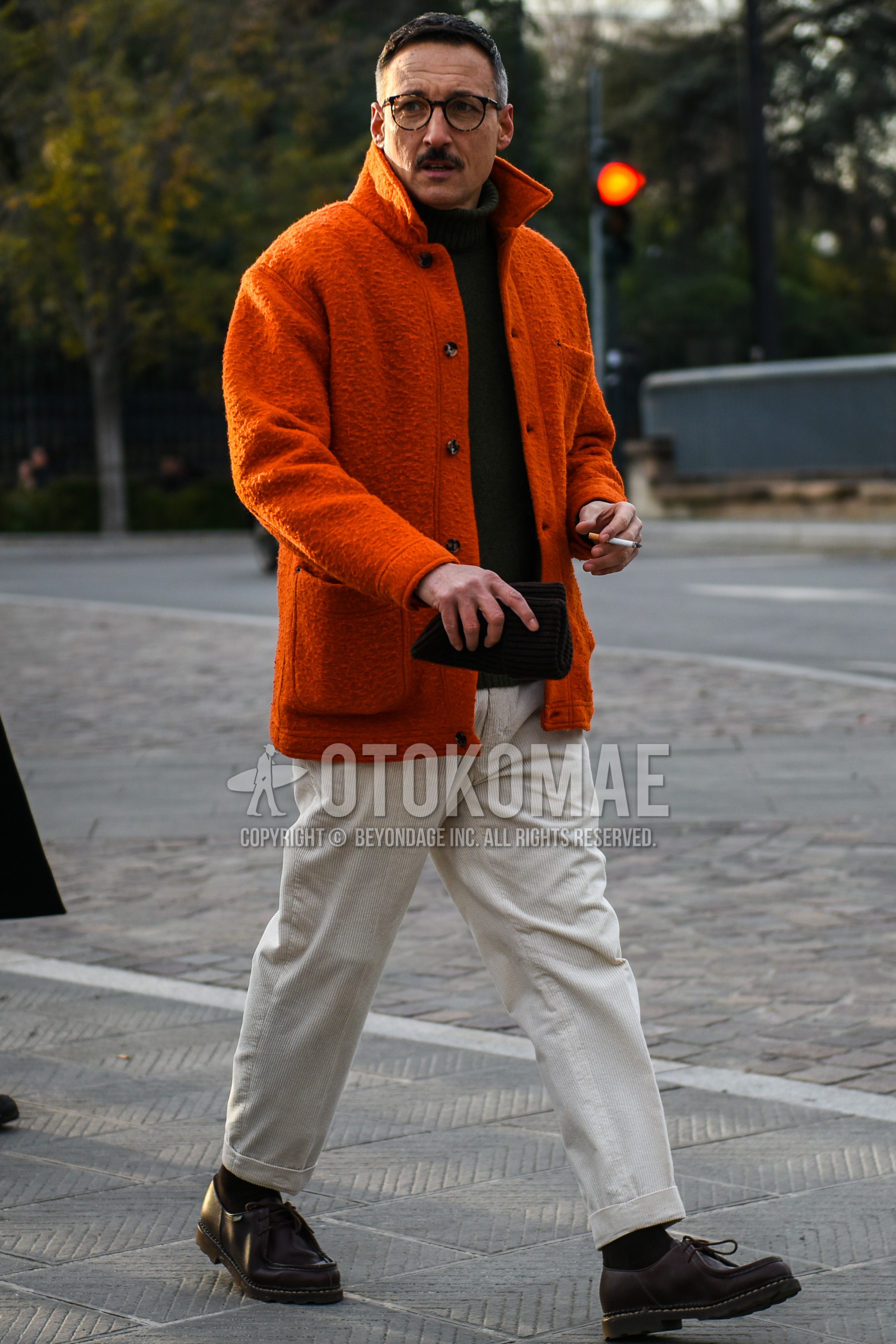 Men's autumn winter outfit with brown tortoiseshell glasses, orange plain fleece jacket, black plain turtleneck knit, beige plain chinos, black plain socks, brown  leather shoes.