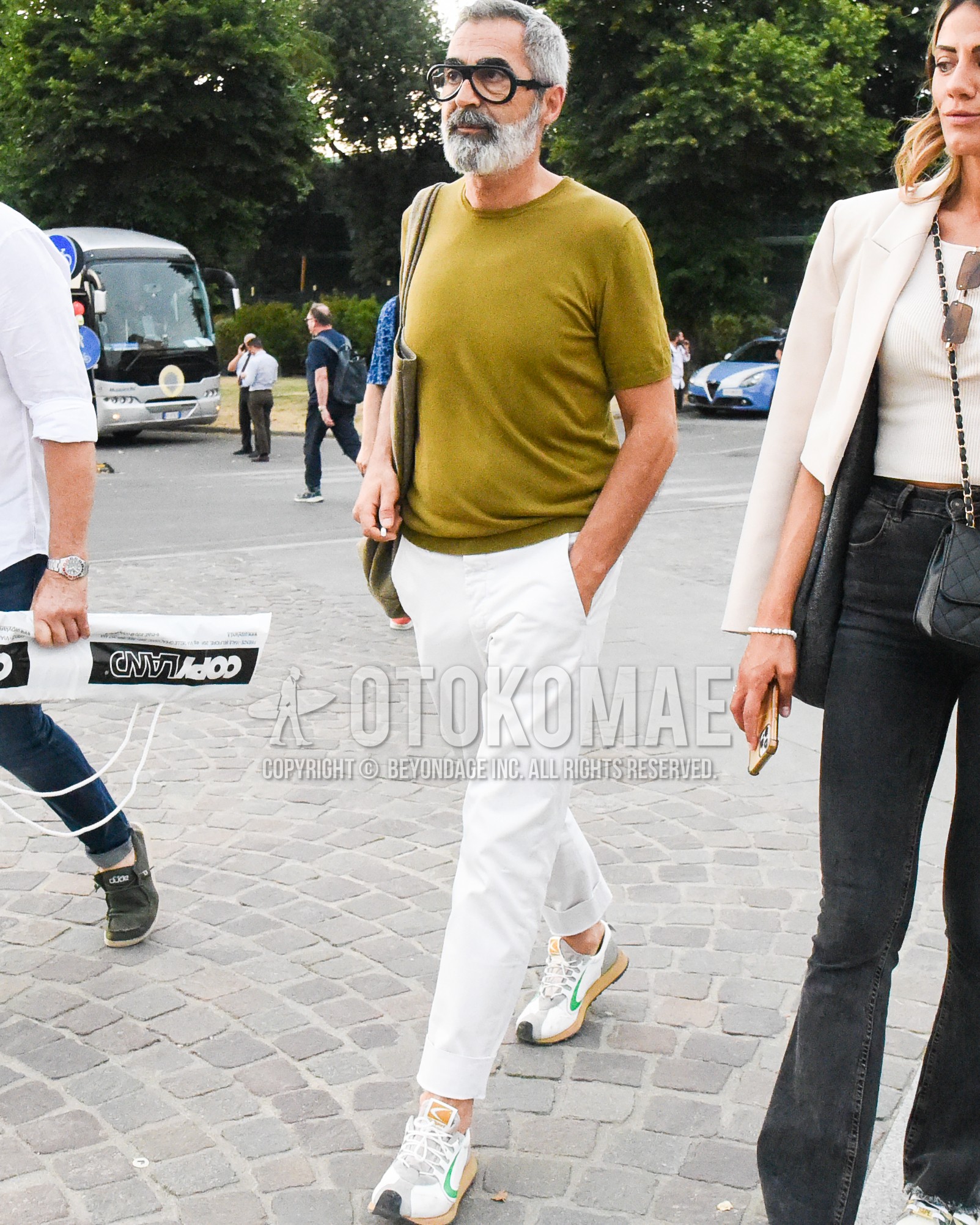 Men's spring summer outfit with clear plain glasses, green plain t-shirt, white plain cotton pants, white low-cut sneakers, olive green plain tote bag.