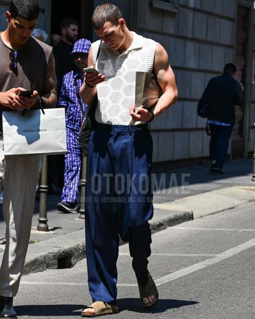 白無地のカジュアルベスト、ブルー無地のスラックス、ベージュレザーサンダルを合わせた春夏のメンズコーデ・着こなし。