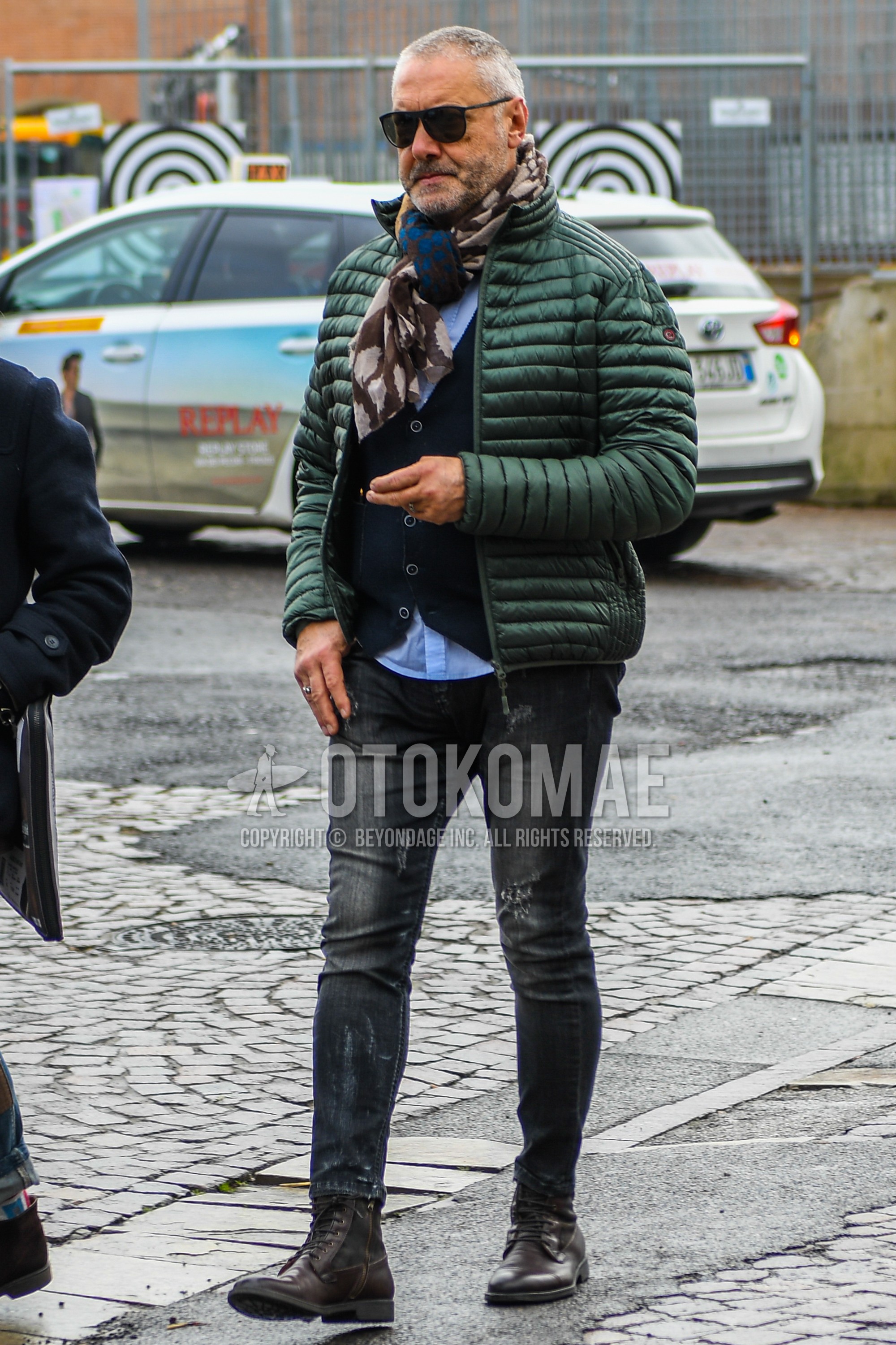 Men's winter outfit with plain sunglasses, brown scarf scarf, green plain down jacket, dark gray plain cardigan, light blue plain shirt, dark gray plain damaged jeans, brown boots.