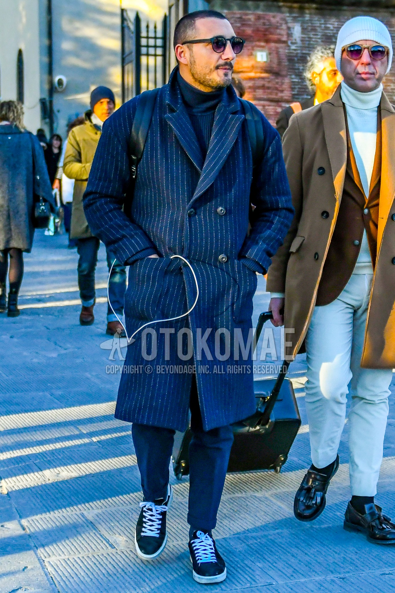 Men's winter outfit with plain sunglasses, navy stripes chester coat, navy plain turtleneck knit, navy plain slacks, black low-cut sneakers.