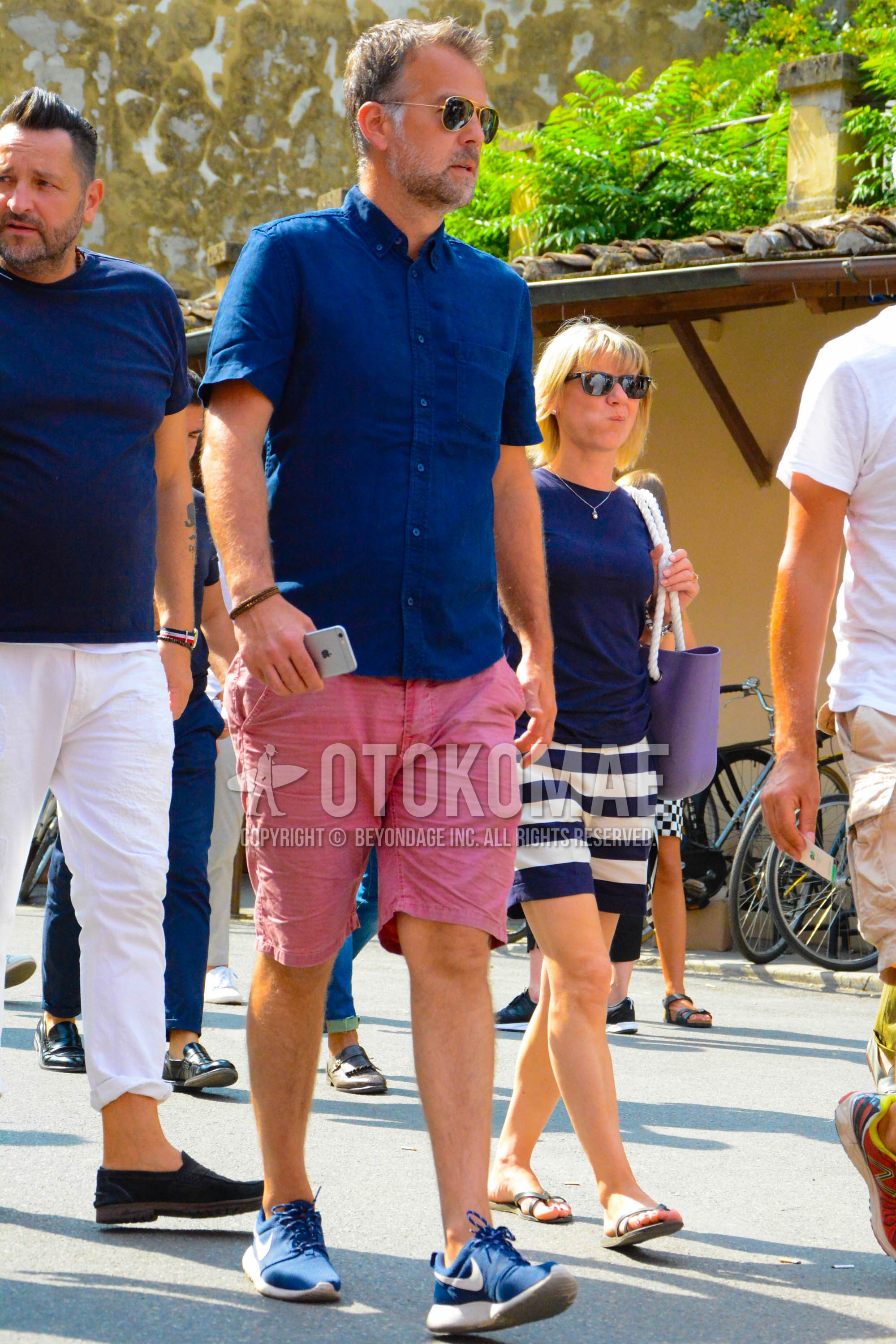 Men's summer outfit with plain sunglasses, blue plain shirt, pink plain short pants, blue low-cut sneakers.