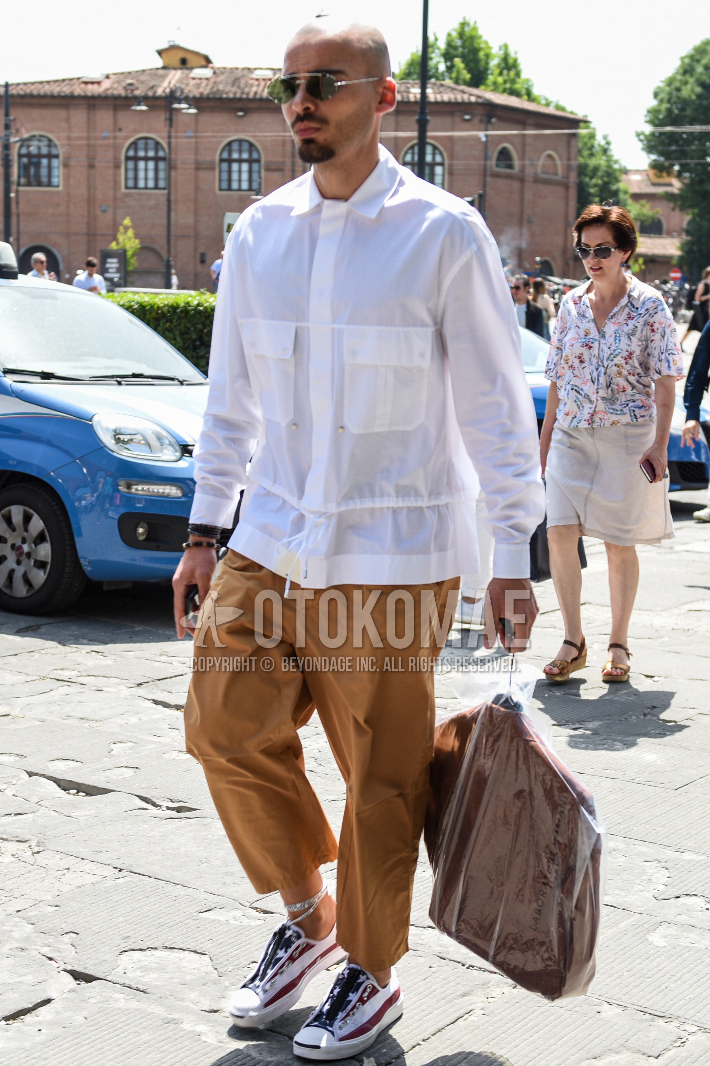 Men's spring summer autumn outfit with silver plain sunglasses, white plain shirt, brown plain ankle pants, white red low-cut sneakers.