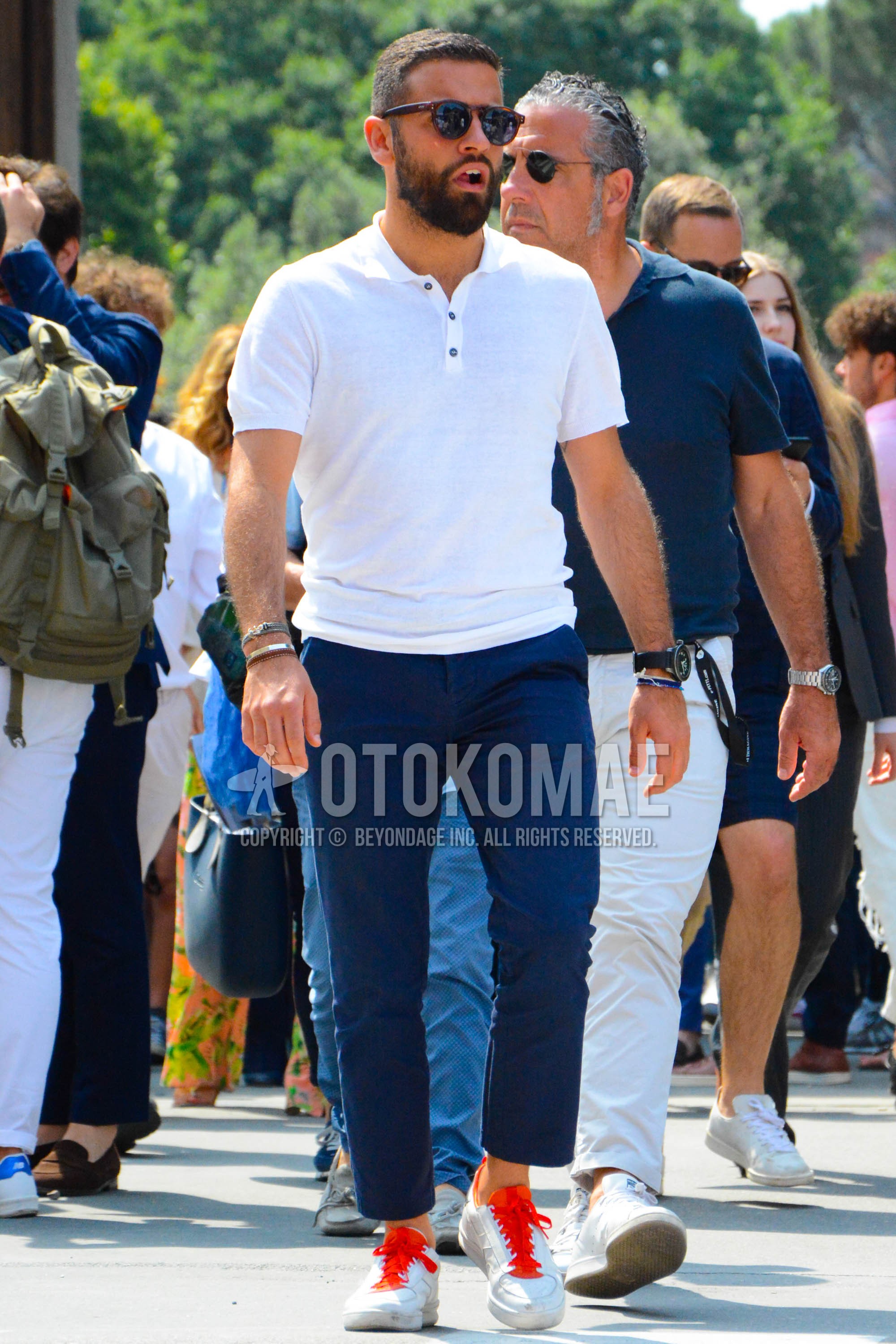 Men's spring summer outfit with brown tortoiseshell sunglasses, white plain polo shirt, navy plain chinos, white low-cut sneakers.