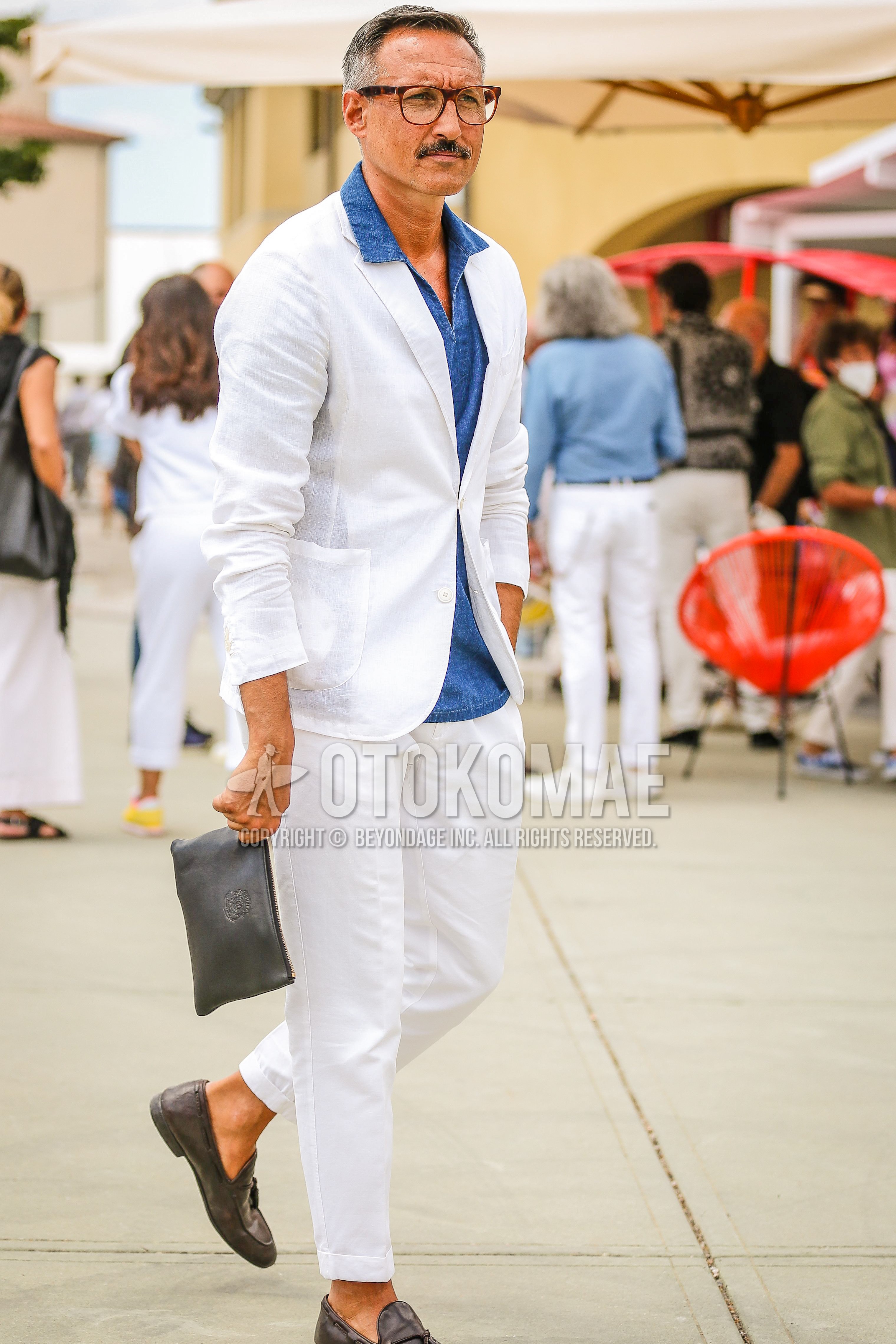 Men's spring summer outfit with brown tortoiseshell glasses, blue plain shirt, gray tassel loafers leather shoes, gray plain clutch bag/second bag/drawstring bag, white plain suit.