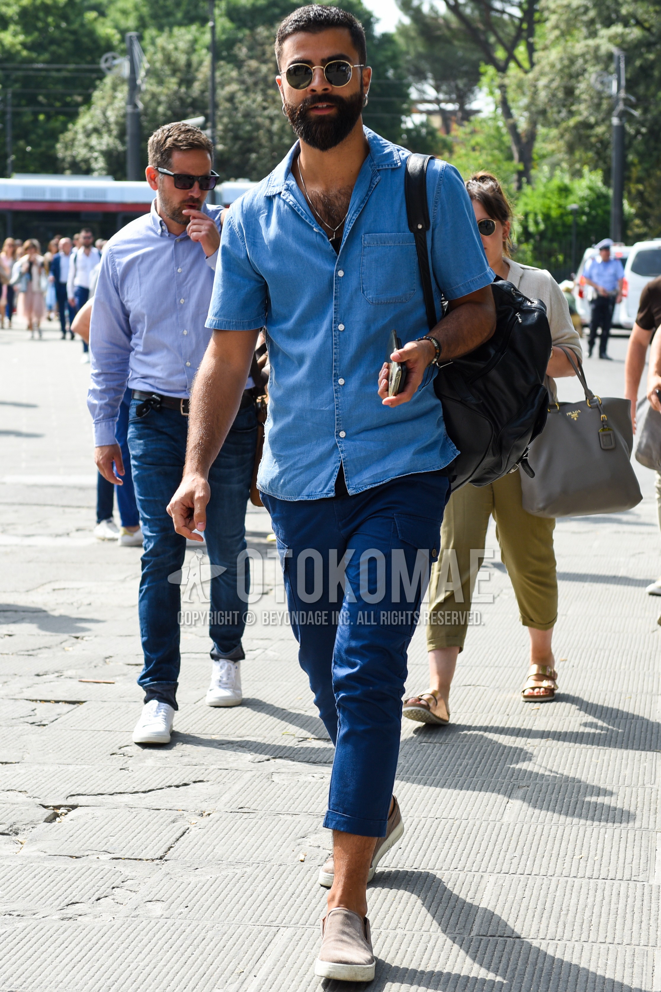 Men's summer outfit with gold plain sunglasses, blue plain denim shirt/chambray shirt, blue plain cargo pants, beige low-cut sneakers.