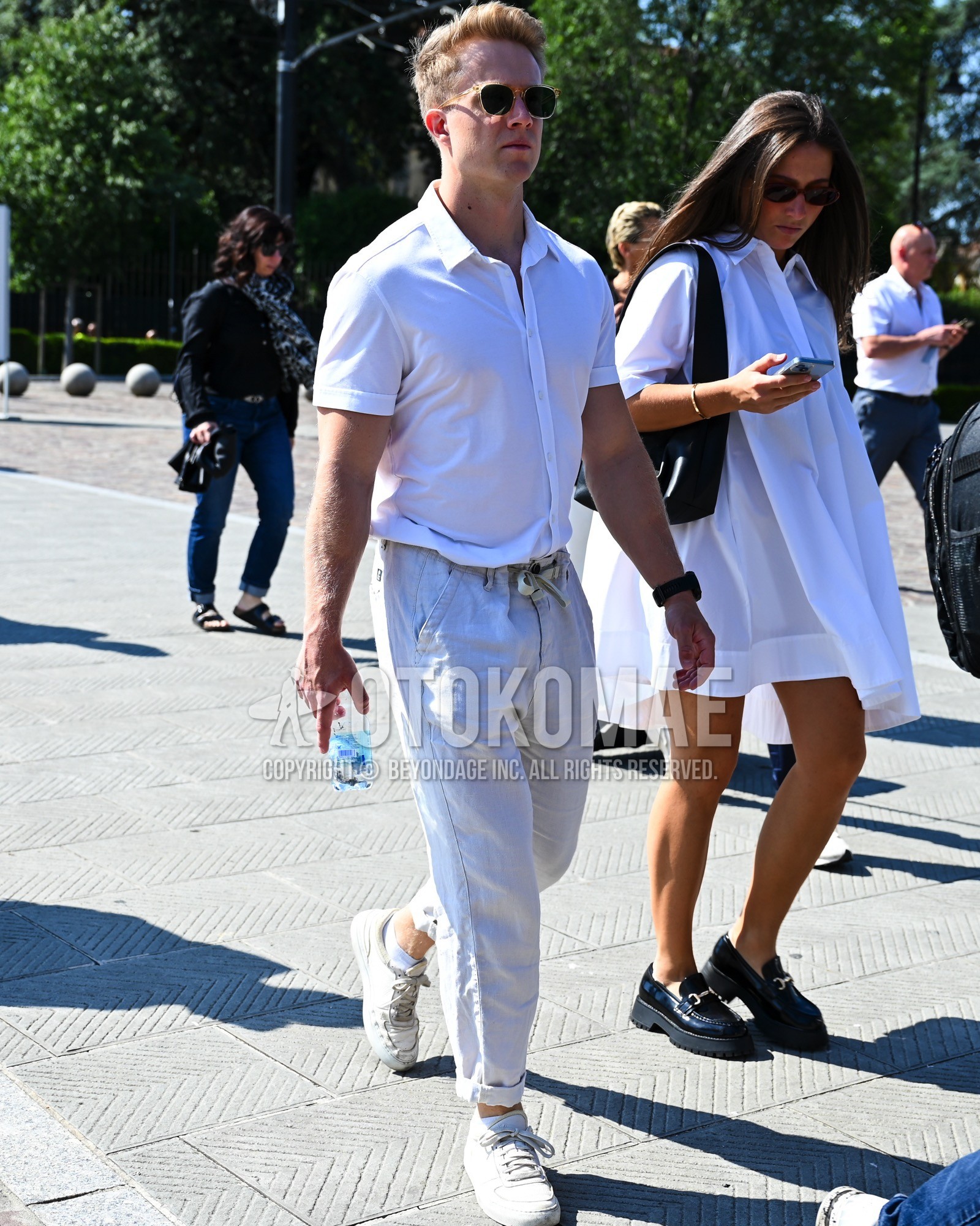 Men's spring summer outfit with black plain sunglasses, white plain shirt, white plain chinos, white low-cut sneakers.