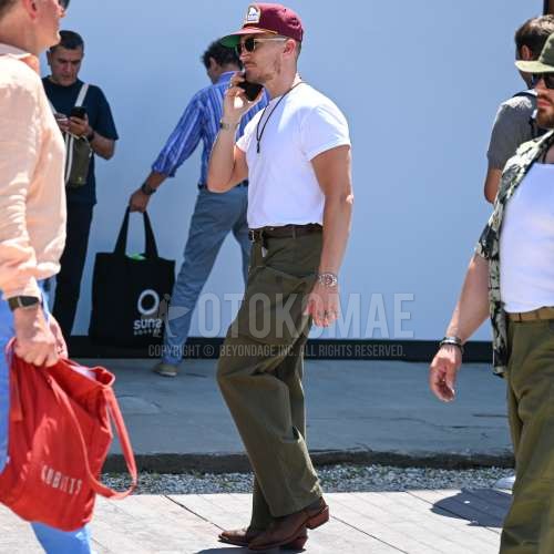 レッドワンポイントのベースボールキャップ、ゴールド無地のサングラス、白無地のTシャツ、ブラウン無地のレザーベルト、グリーンストライプのカーゴパンツ、ブラウンのブーツを合わせた夏春のメンズコーデ・着こなし。