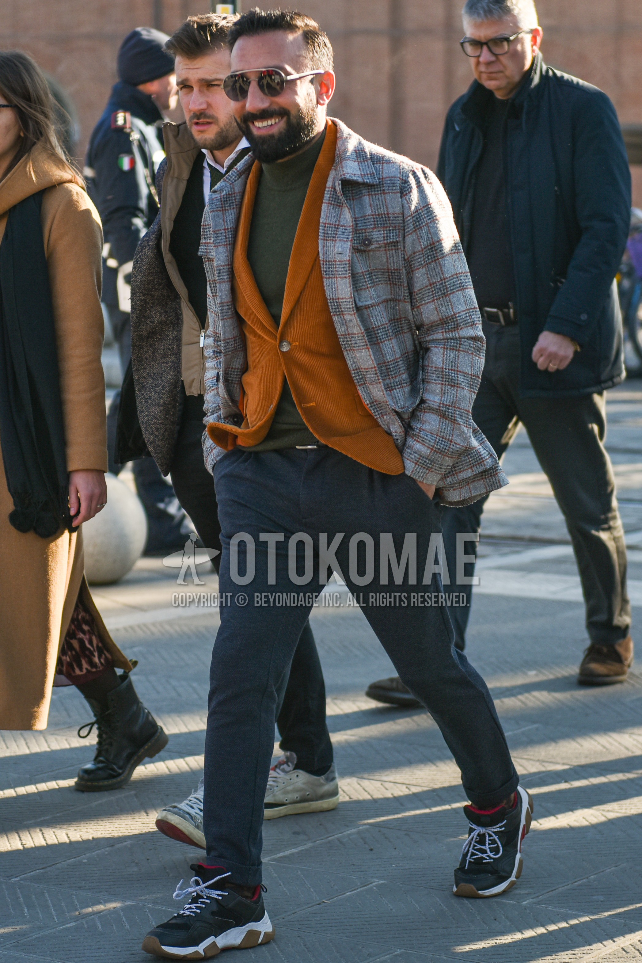 Men's autumn winter outfit with gold plain sunglasses, gray check shirt jacket, brown plain tailored jacket, gray plain turtleneck knit, gray plain slacks, gray low-cut sneakers.