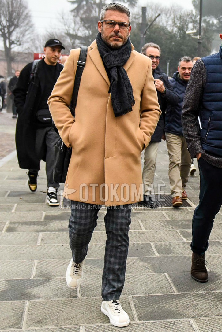 Men's autumn winter outfit with plain glasses, gray scarf scarf, beige plain chester coat, gray black check slacks, white low-cut sneakers.