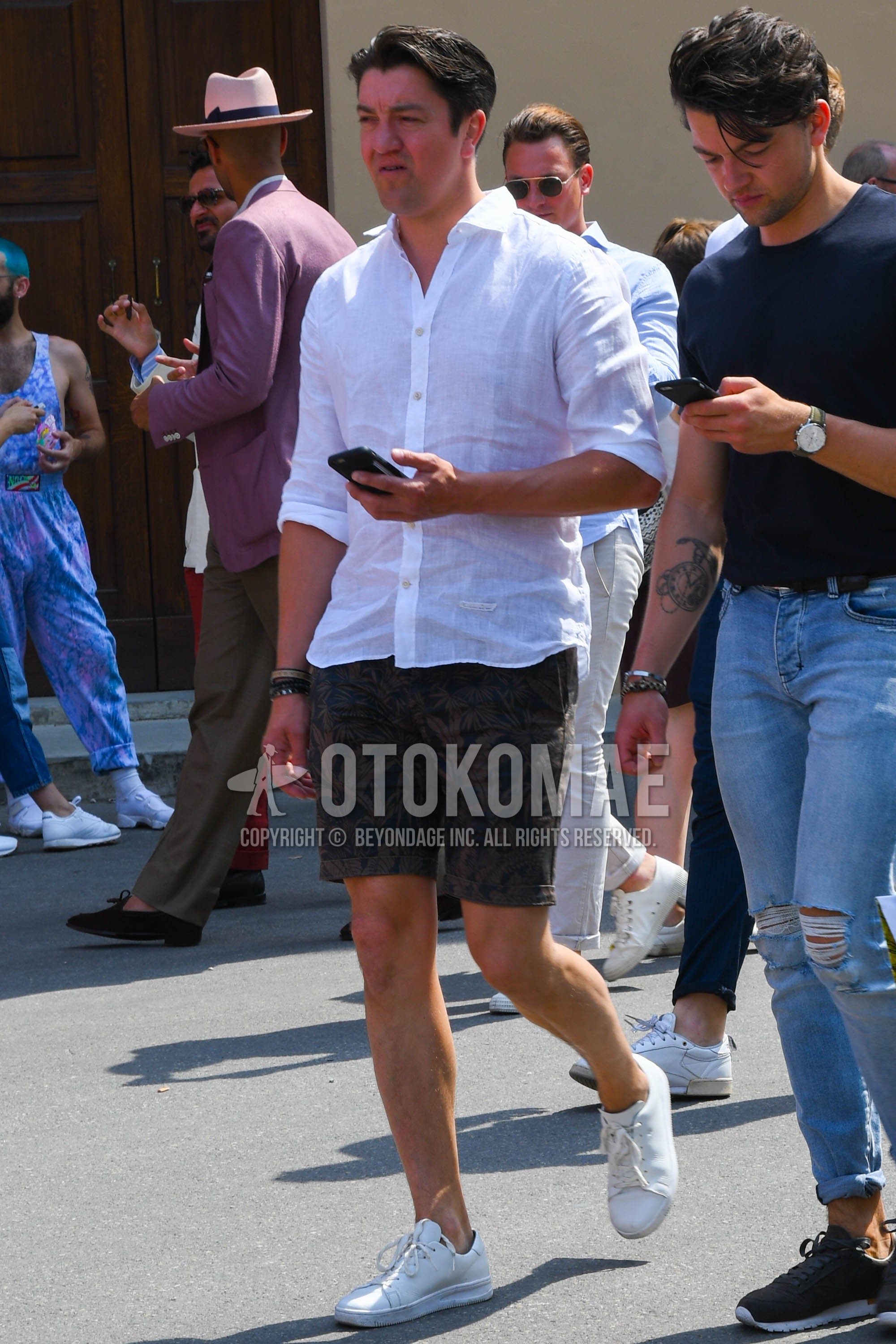 Men's spring summer outfit with white plain shirt, olive green botanical short pants, white low-cut sneakers.