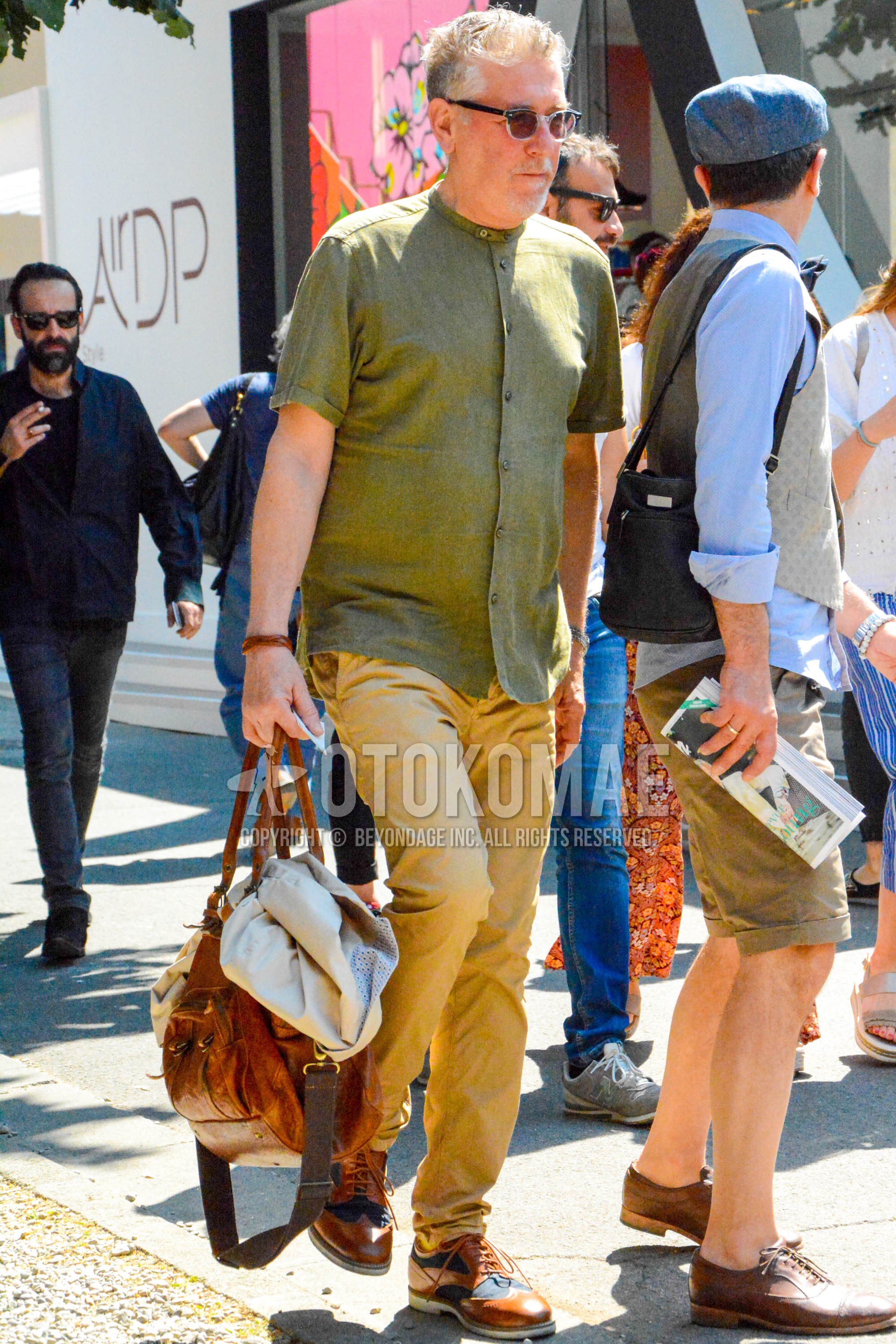 Men's summer outfit with plain sunglasses, olive green plain shirt, beige plain chinos, brown brogue shoes leather shoes, brown plain boston bag.