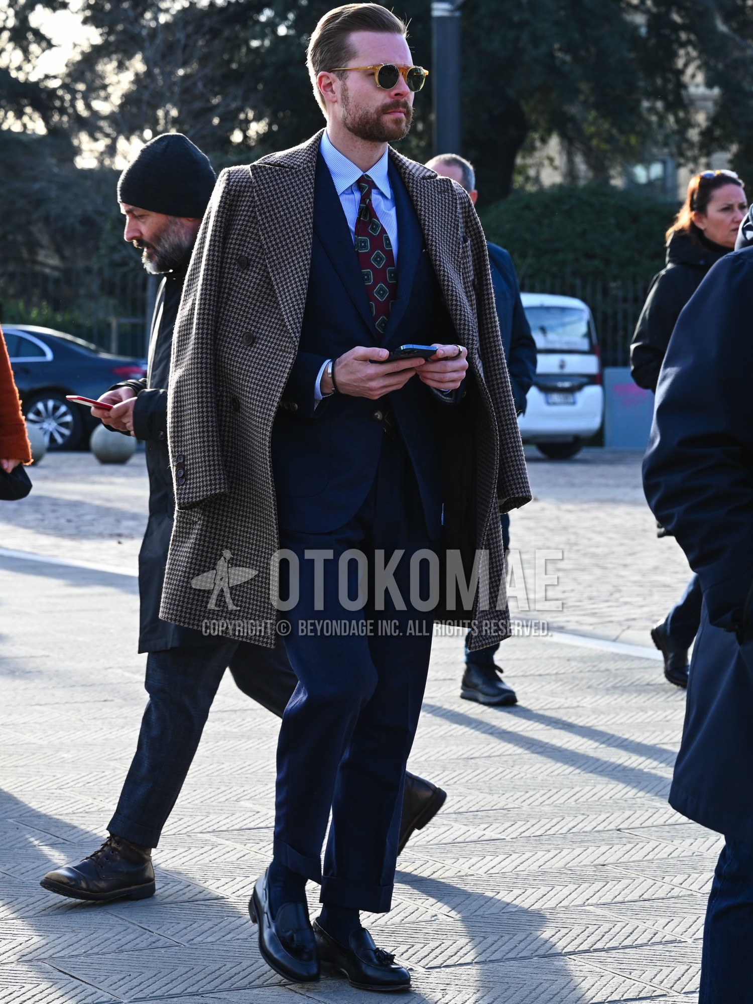 Men's autumn winter outfit with brown plain sunglasses, gray check chester coat, blue stripes shirt, navy plain socks, black tassel loafers leather shoes, navy plain suit, red graphic necktie.