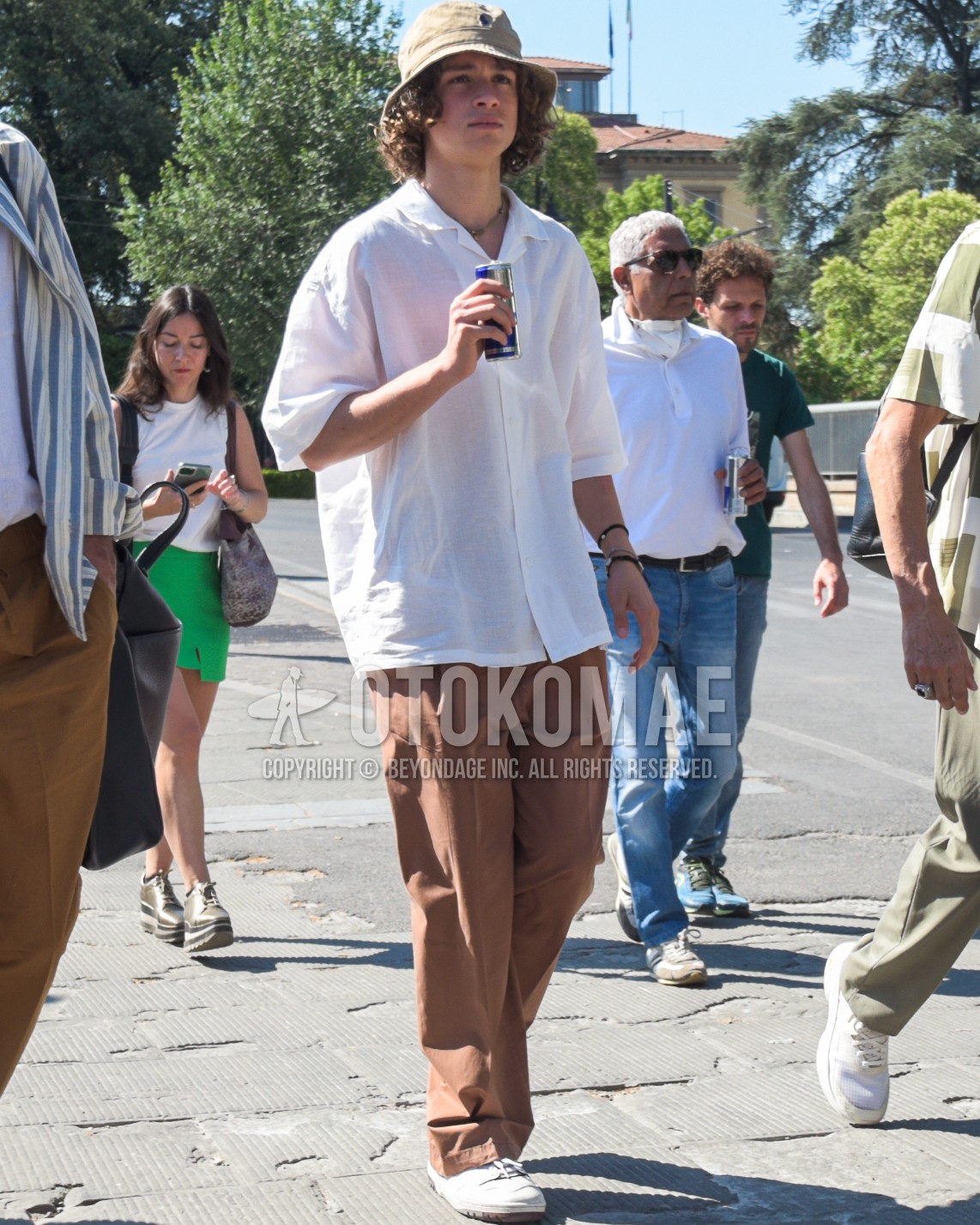 Men's spring summer outfit with beige one point bucket hat, white plain shirt, brown plain wide pants, white low-cut sneakers.