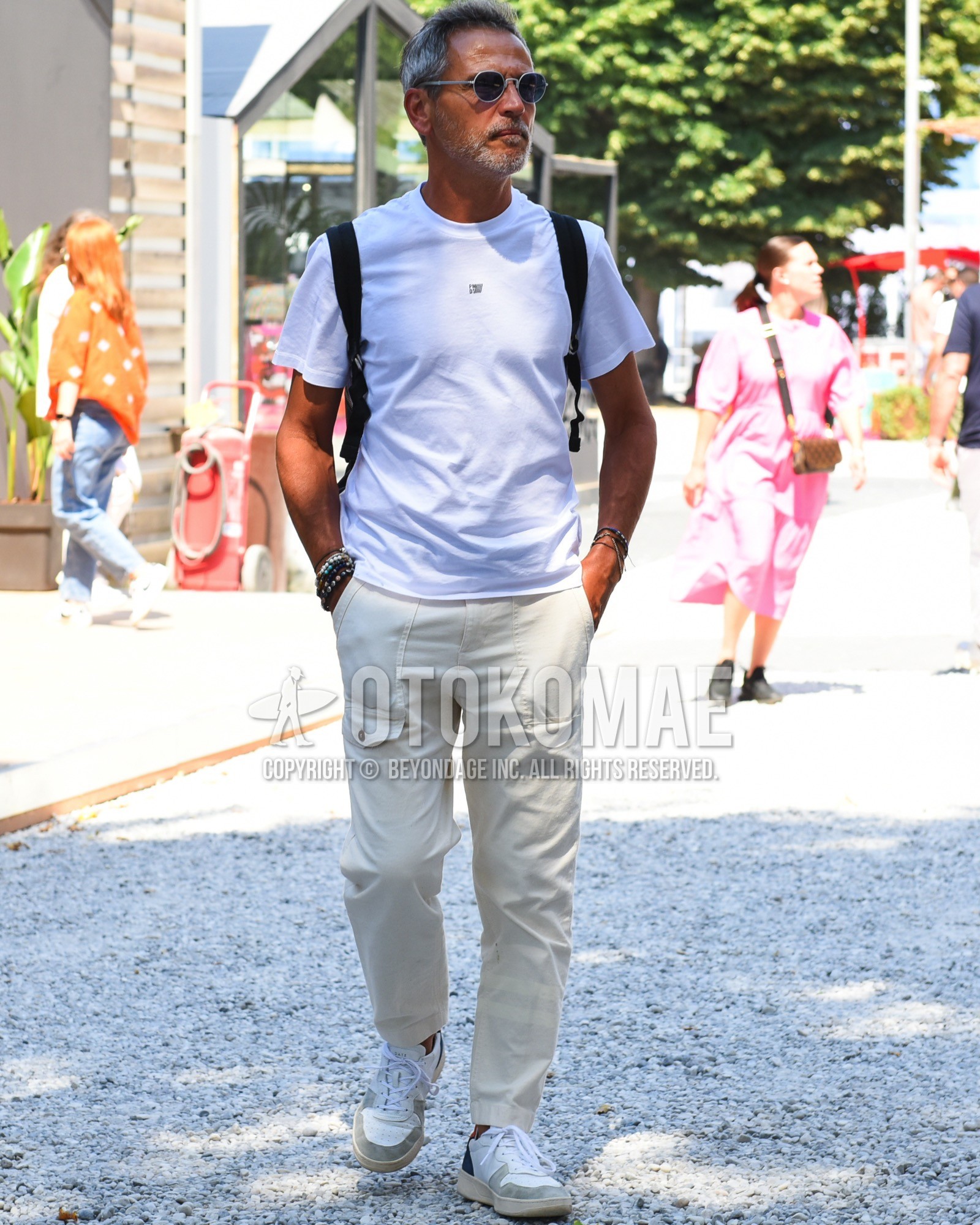 Men's spring summer outfit with silver plain sunglasses, white one point t-shirt, white plain baker pants, white gray low-cut sneakers, black plain backpack.