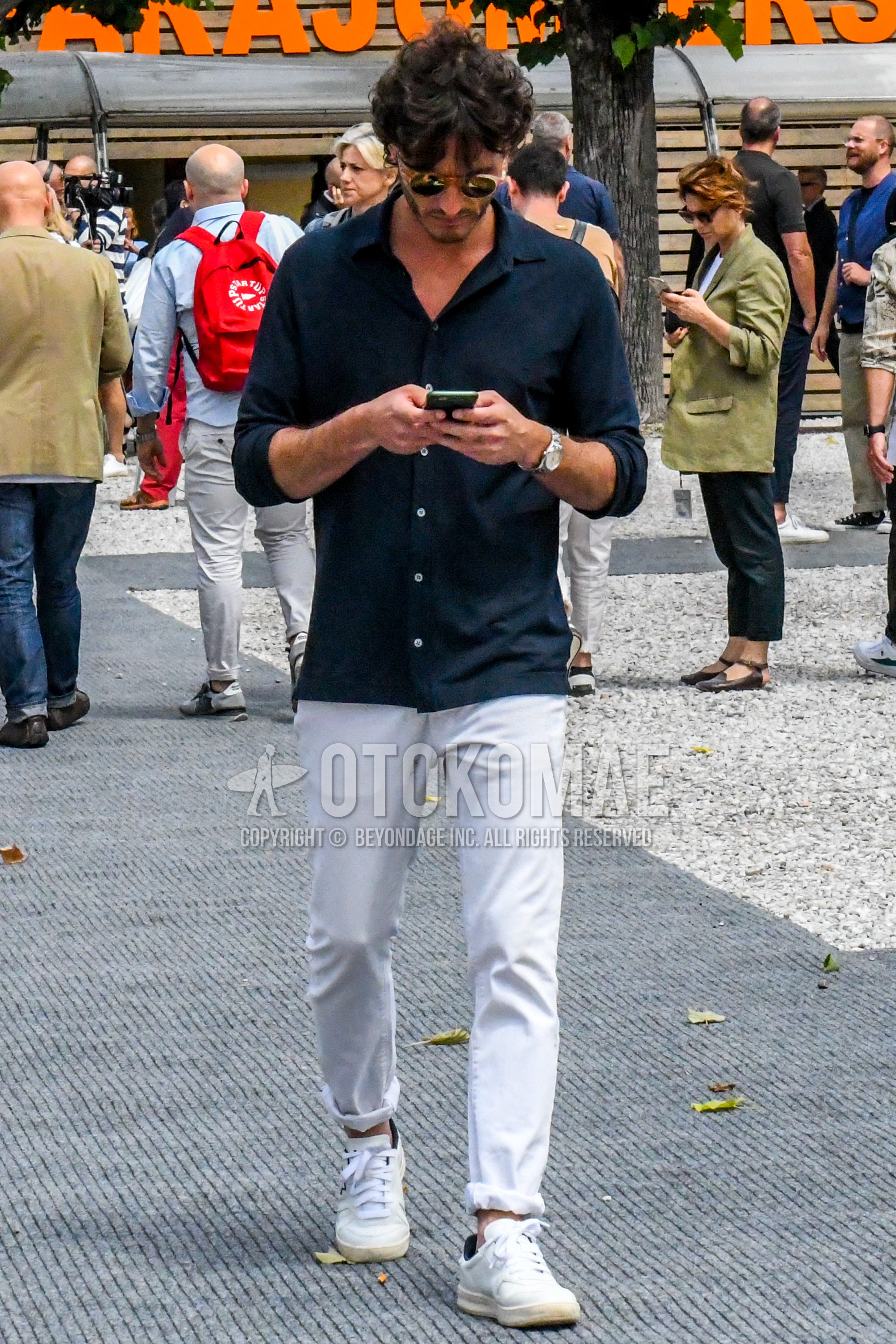 Men's summer outfit with black yellow plain sunglasses, navy plain shirt, white plain chinos, white low-cut sneakers.