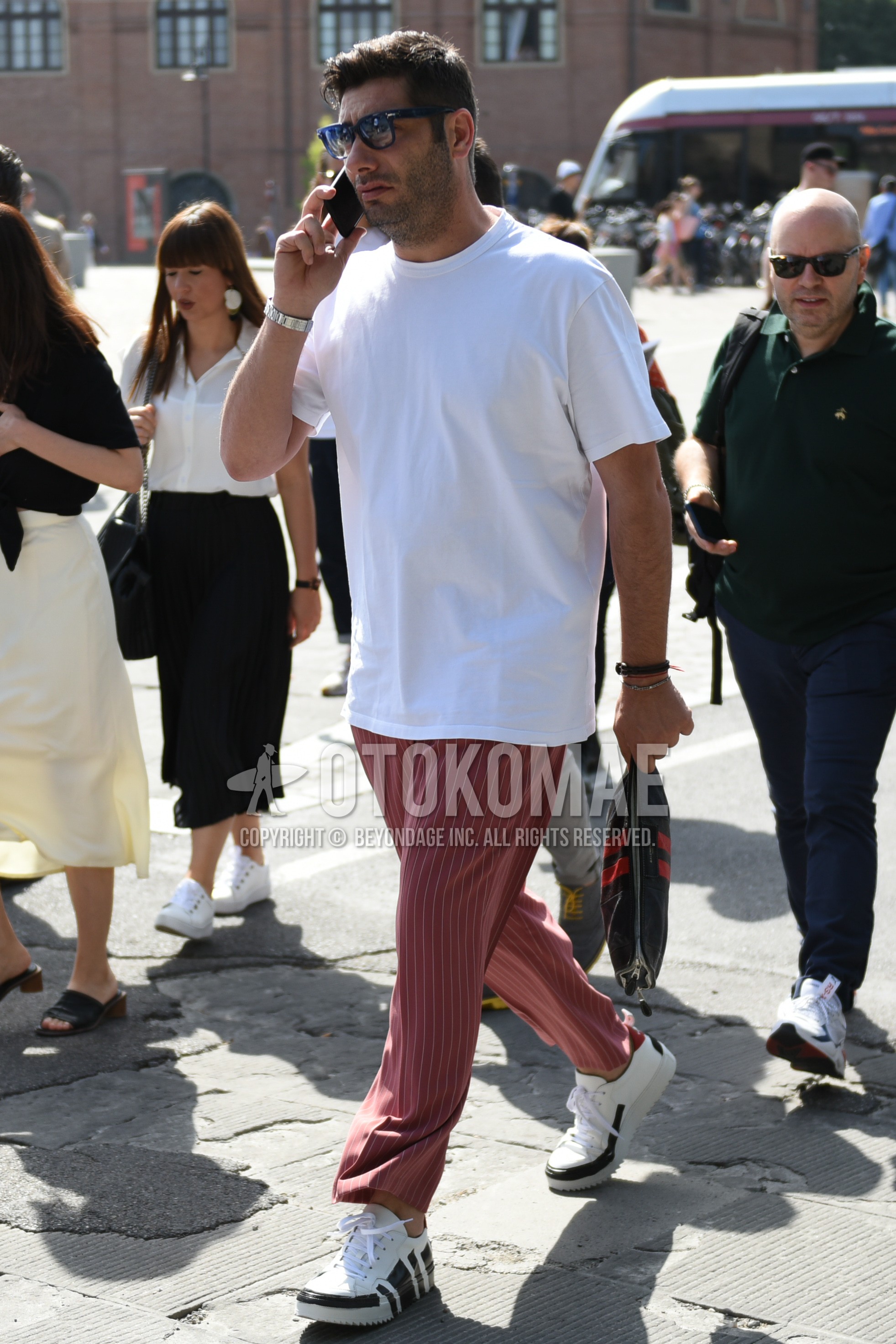 Men's summer outfit with black plain sunglasses, white plain t-shirt, red stripes wide pants, white low-cut sneakers, dark gray graphic clutch bag/second bag/drawstring bag.