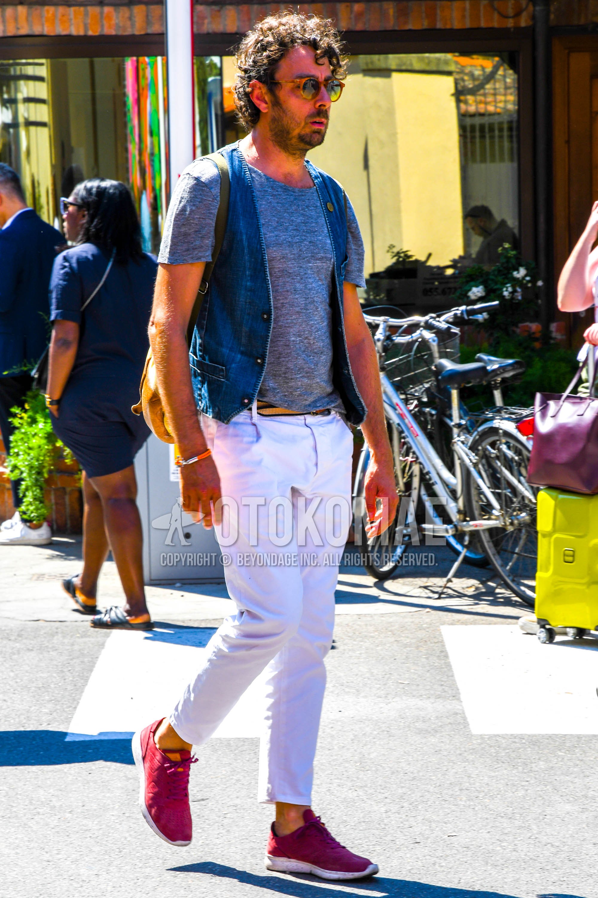Men's spring summer outfit with tortoiseshell sunglasses, blue plain gilet, gray plain t-shirt, white plain cotton pants, plain ankle pants, red low-cut sneakers.