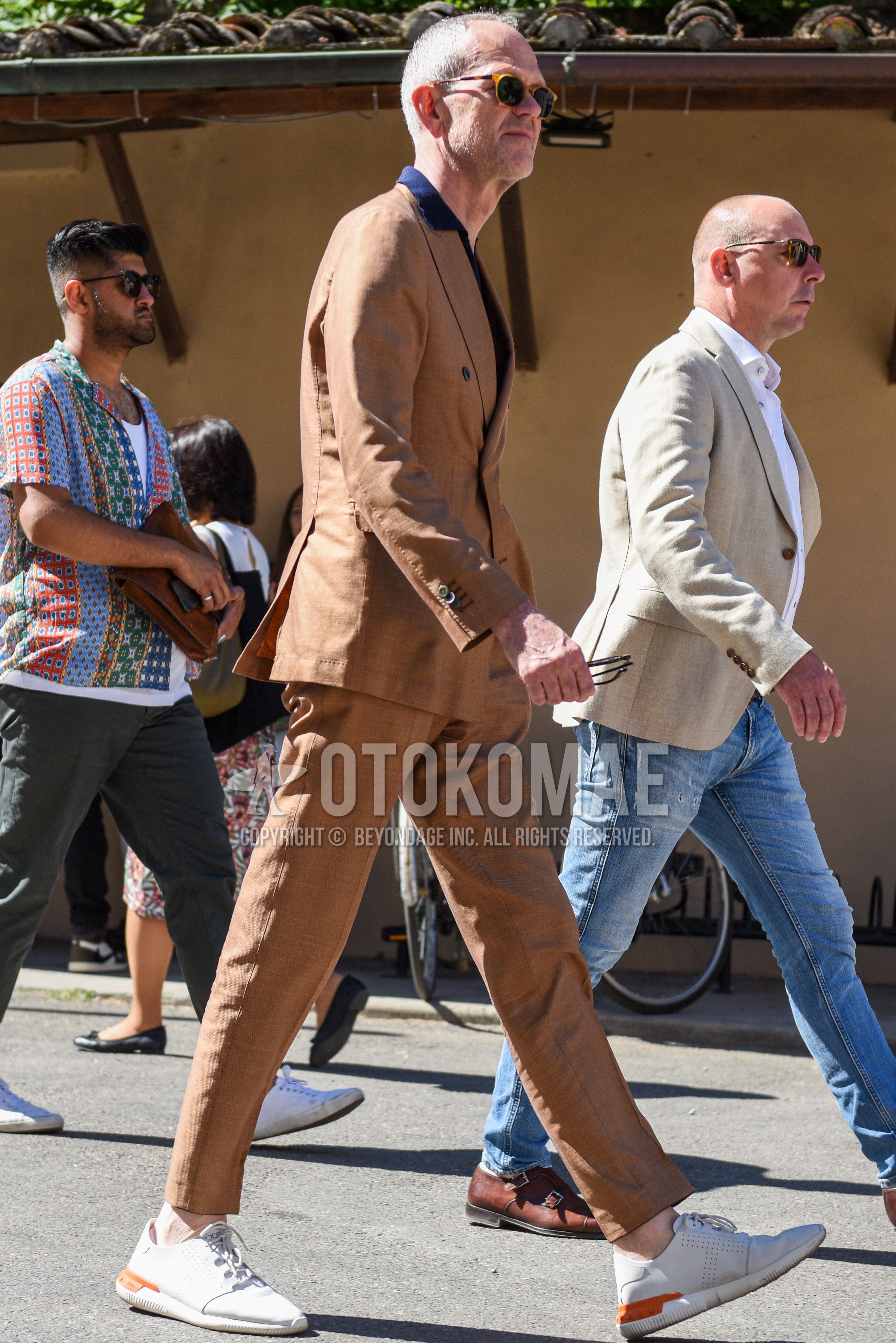 Men's spring autumn outfit with beige plain sunglasses, navy plain shirt, white low-cut sneakers, beige plain suit.