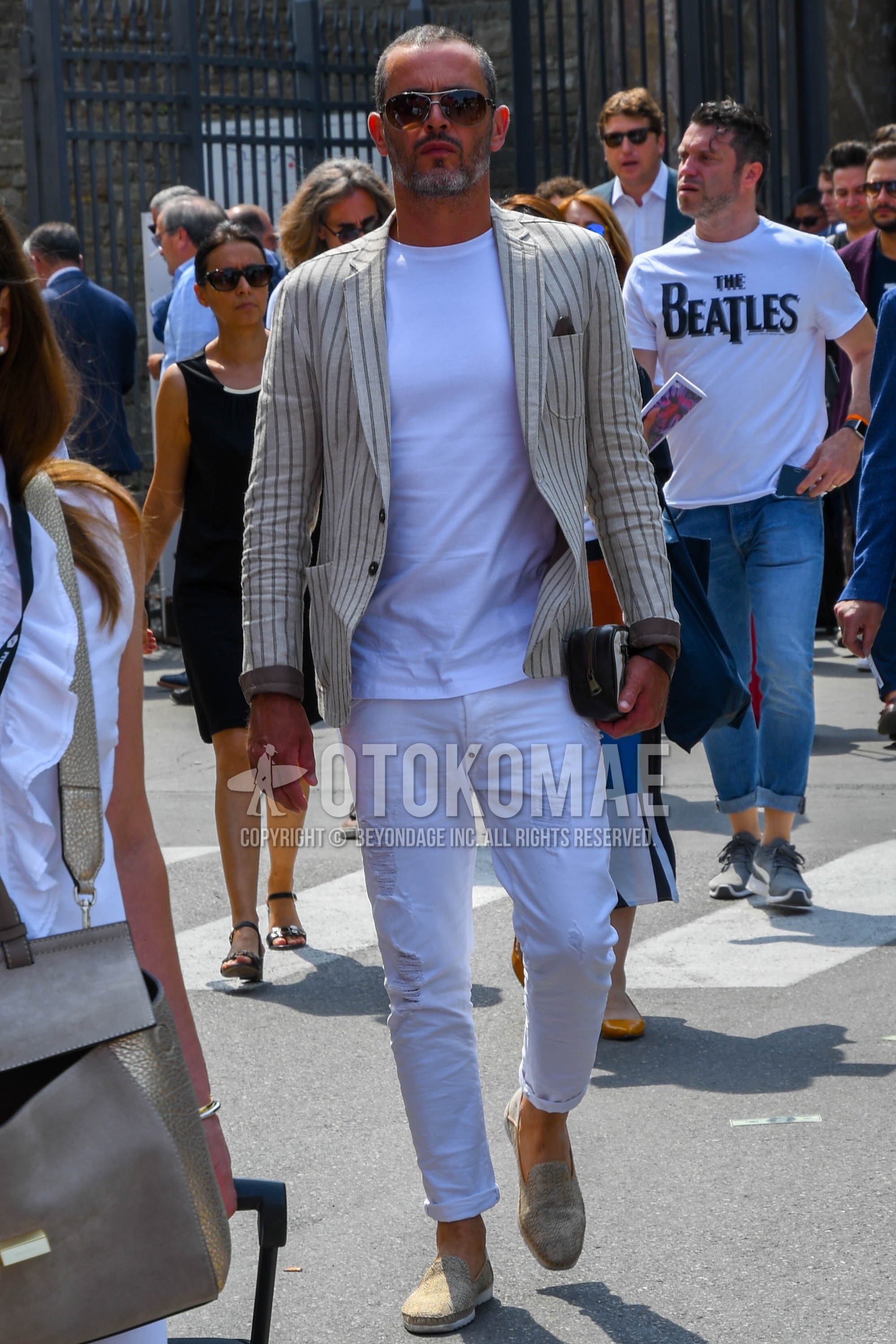 Men's spring summer autumn outfit with silver plain sunglasses, beige stripes tailored jacket, white plain t-shirt, white plain damaged jeans, beige slip-on sneakers, brown plain clutch bag/second bag/drawstring bag.