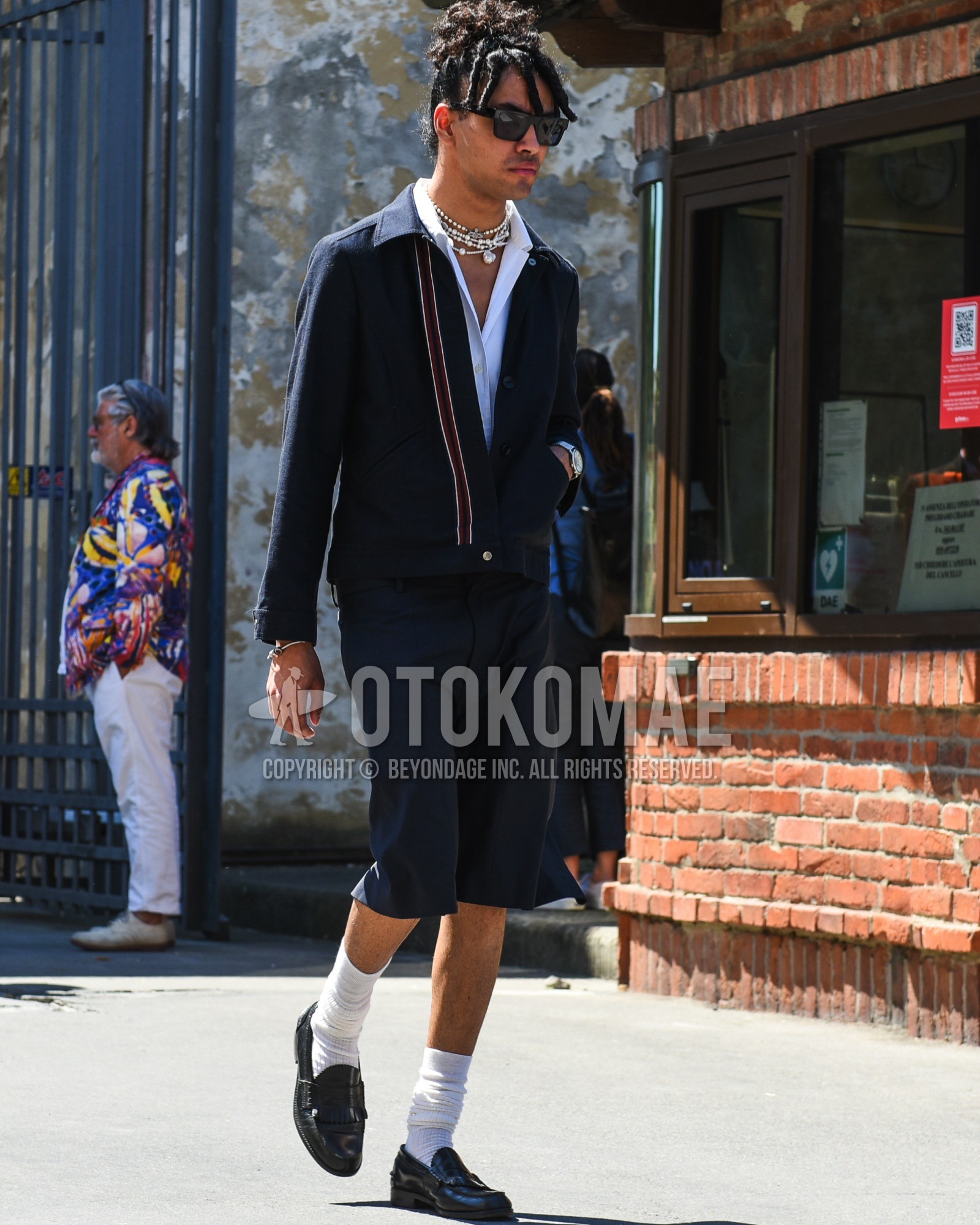 Men's spring summer outfit with black plain sunglasses, navy plain shirt jacket, white plain shirt, navy plain short pants, white plain socks, black coin loafers leather shoes.
