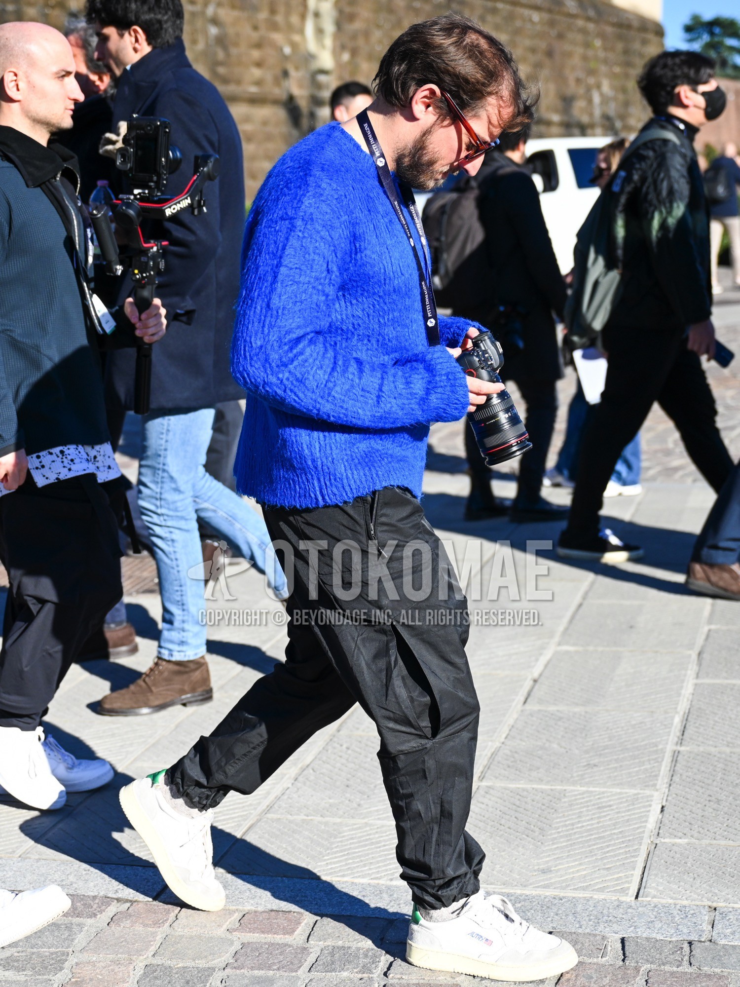 Men's spring autumn winter outfit with brown tortoiseshell sunglasses, blue plain sweater, black plain cargo pants, white plain socks, white low-cut sneakers.