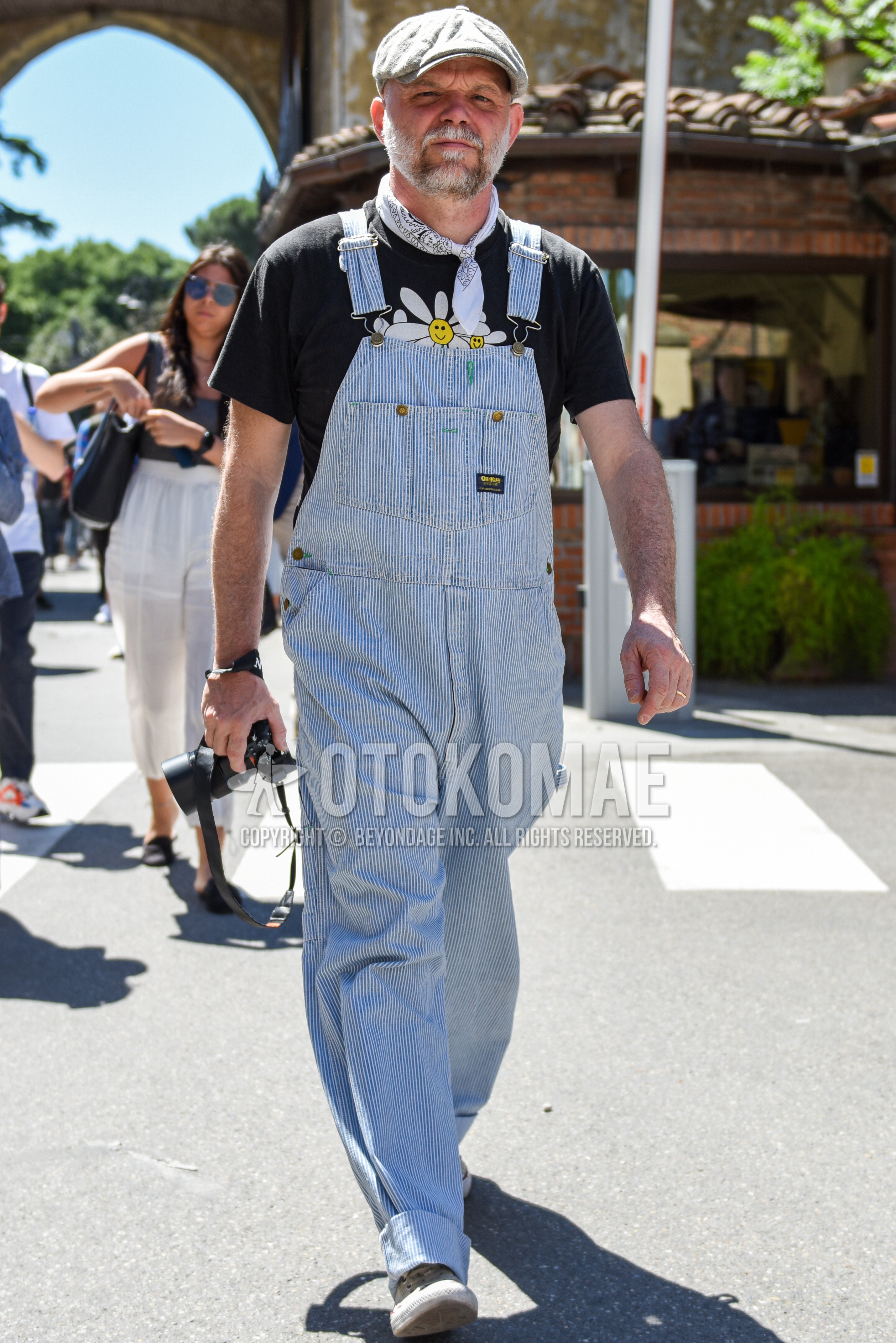 Men's spring summer outfit with gray plain cap, light blue stripes jumpsuit, black graphic t-shirt, white high-cut sneakers.