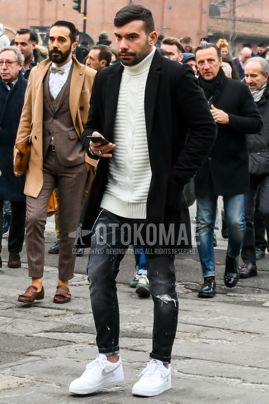 Men's winter outfit with black plain chester coat, white plain turtleneck knit, dark gray plain damaged jeans, white low-cut sneakers.