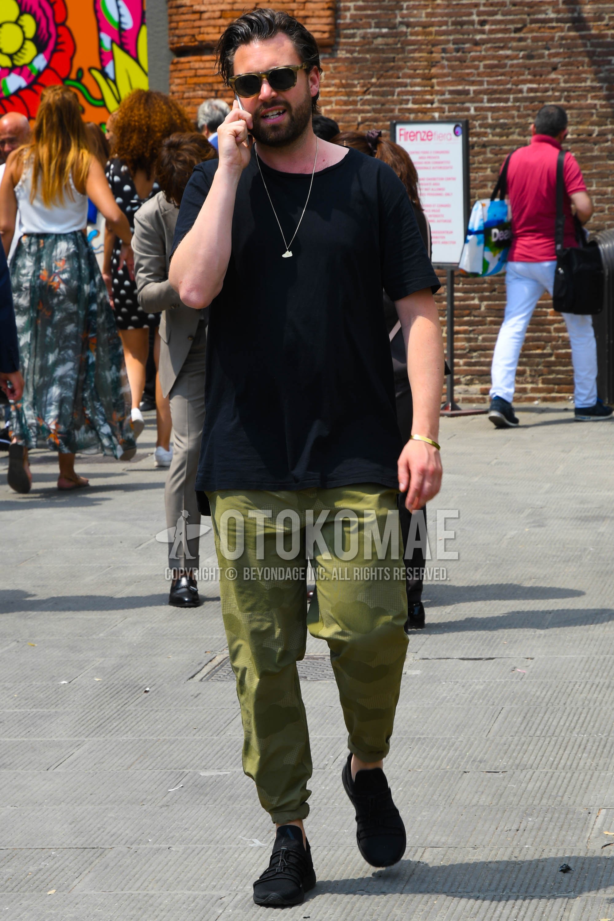 Men's spring summer outfit with beige tortoiseshell sunglasses, black plain t-shirt, olive green camouflage chinos, black low-cut sneakers.