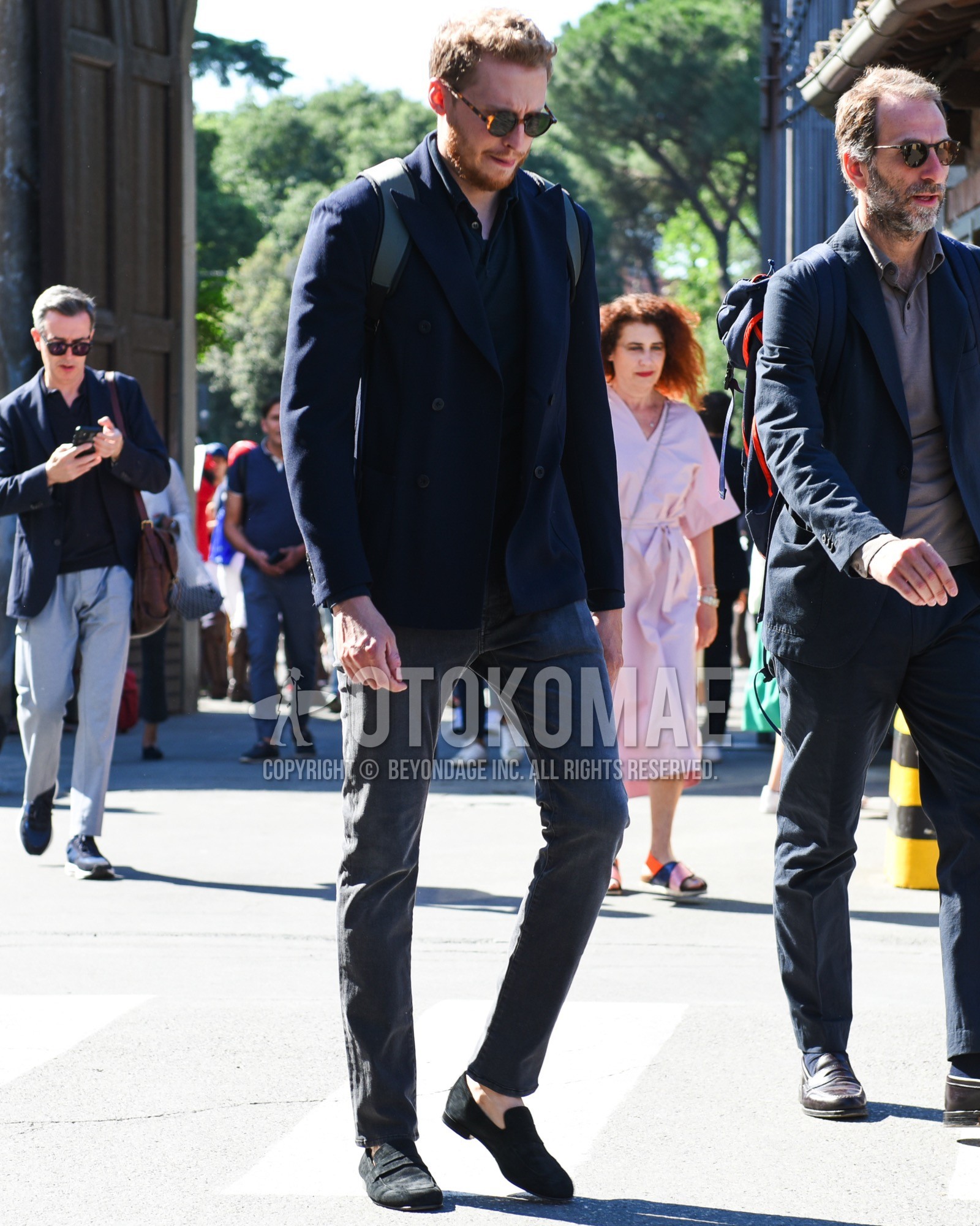 Men's spring summer outfit with brown tortoiseshell sunglasses, navy plain tailored jacket, black plain polo shirt, gray plain denim/jeans, black coin loafers leather shoes, black plain backpack.