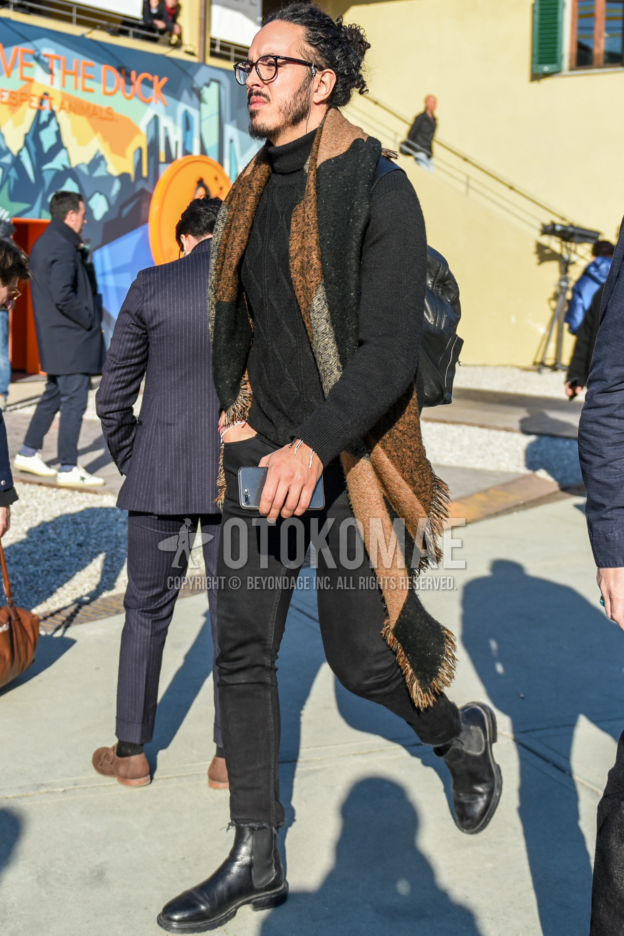 Men's spring autumn outfit with black plain glasses, multi-color scarf scarf, black plain turtleneck knit, black plain denim/jeans, black plain cropped pants, black side-gore boots, black plain backpack.