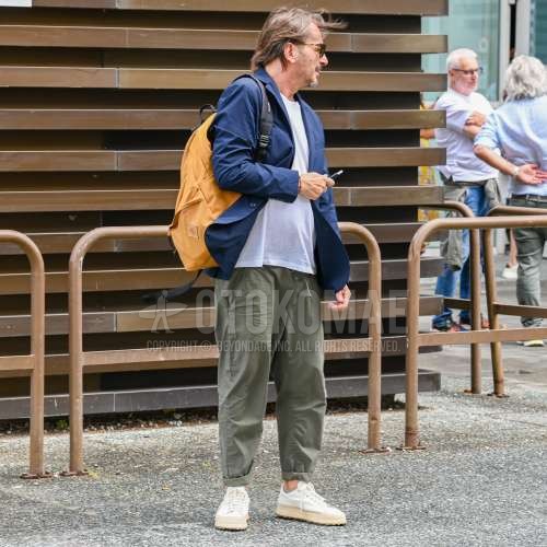 ブラウンべっ甲のサングラス、ネイビー無地のテーラードジャケット、白無地のTシャツ、オリーブグリーン無地のイージーパンツ、白ローカットのスニーカー、イエロー無地のバックパックを合わせた夏春のメンズコーデ・着こなし。