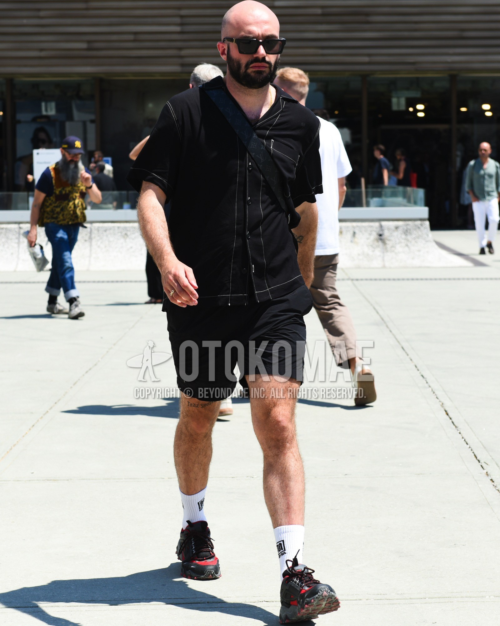 Men's spring summer outfit with black plain sunglasses, black plain shirt, black plain short pants, white one point socks, black low-cut sneakers, black plain shoulder bag.