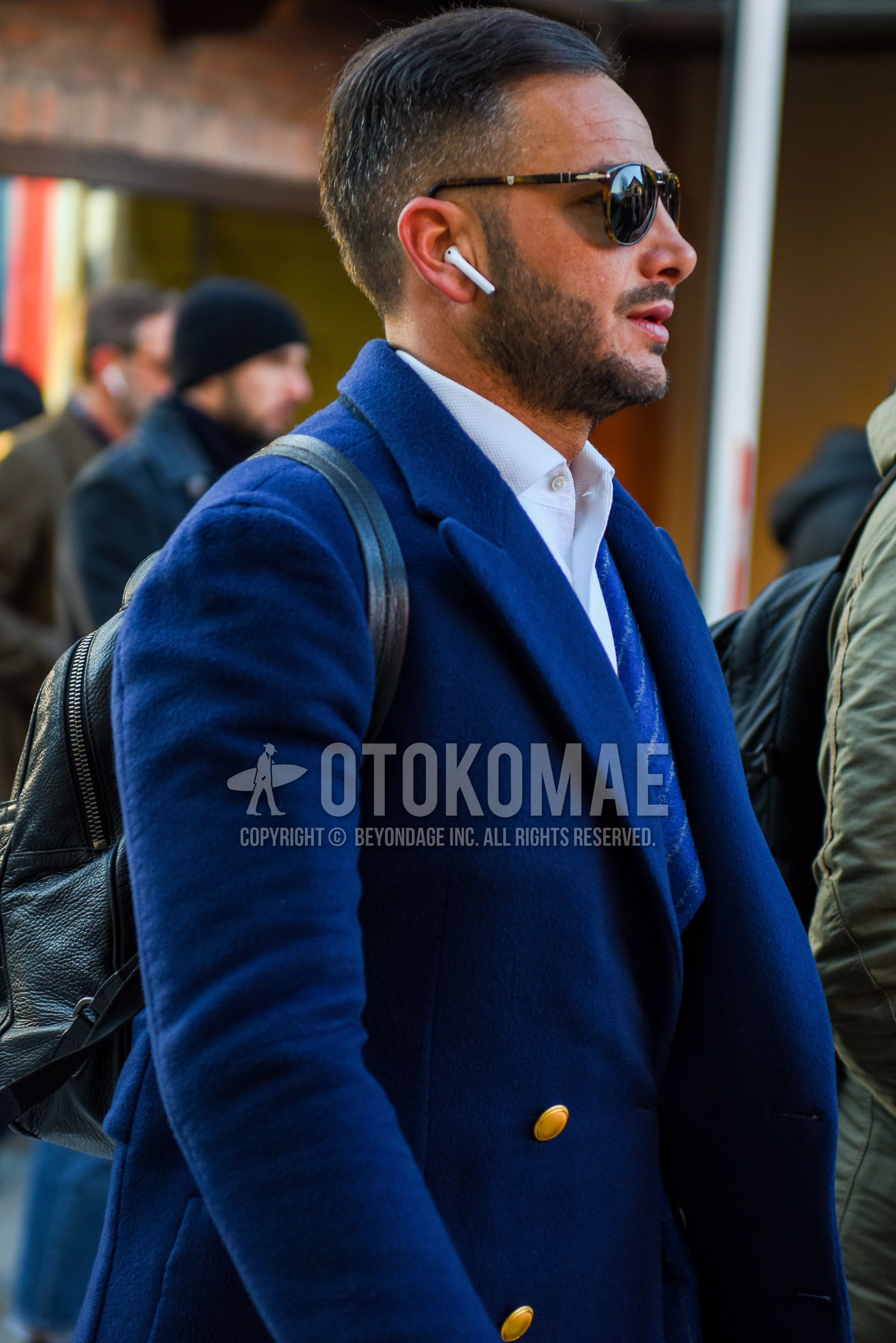 Men's autumn winter outfit with brown tortoiseshell sunglasses, navy plain chester coat, white plain shirt, navy stripes tailored jacket, black plain backpack.