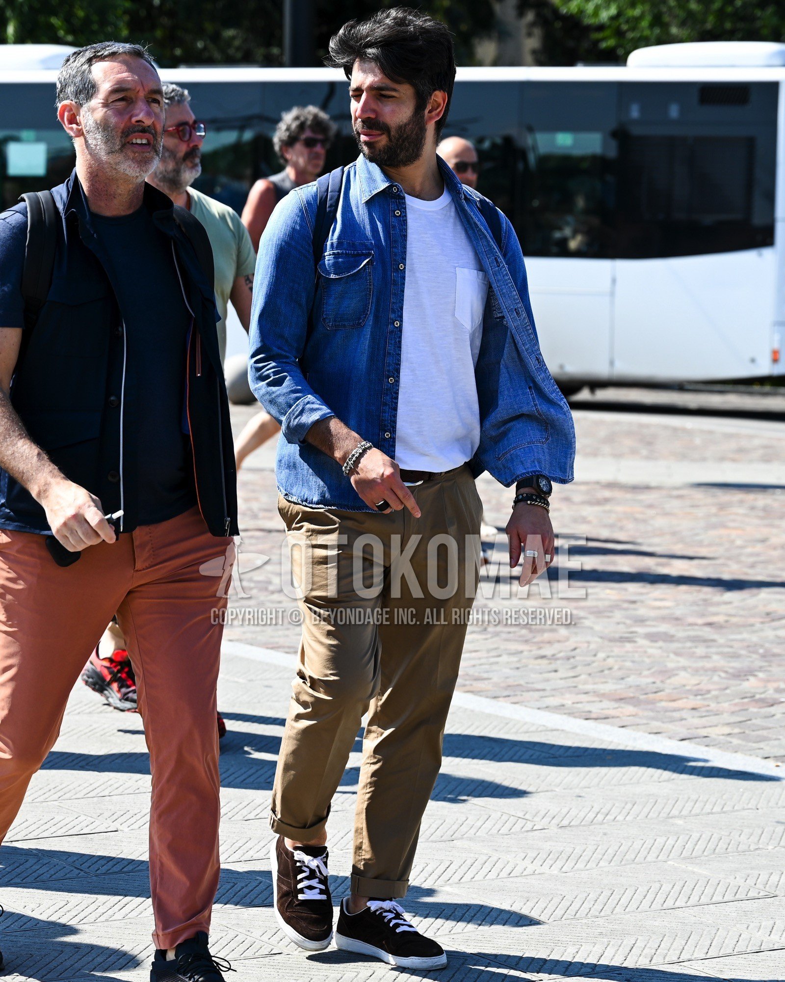 Men's spring summer autumn outfit with blue plain denim shirt/chambray shirt, white plain t-shirt, brown plain leather belt, brown plain chinos, brown low-cut sneakers, navy plain backpack.