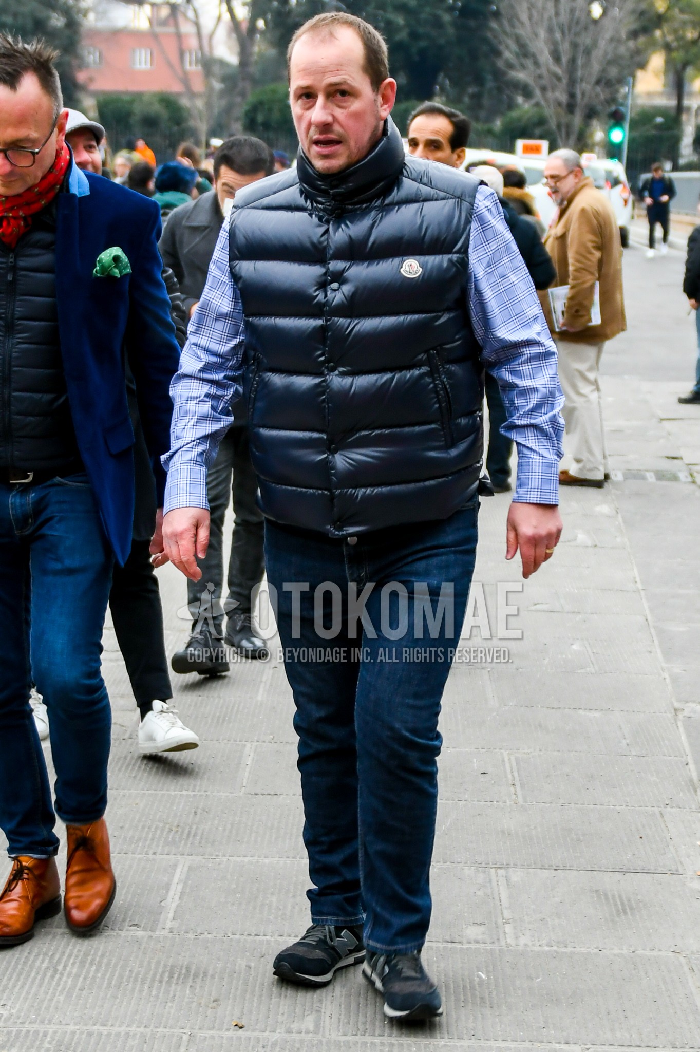 Men's autumn winter outfit with black plain down jacket, blue check shirt, blue plain denim/jeans, black low-cut sneakers.