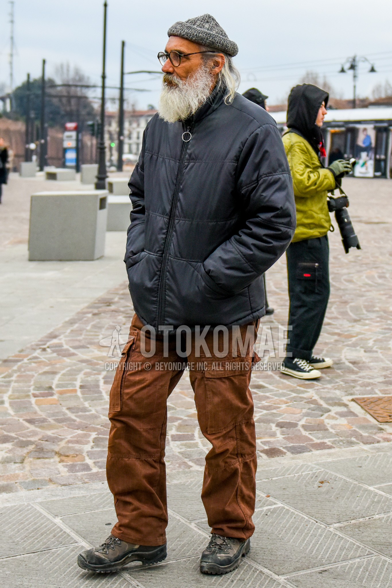 Men's winter outfit with gray plain knit cap, plain glasses, black plain down jacket, brown plain cargo pants, dark gray  boots.