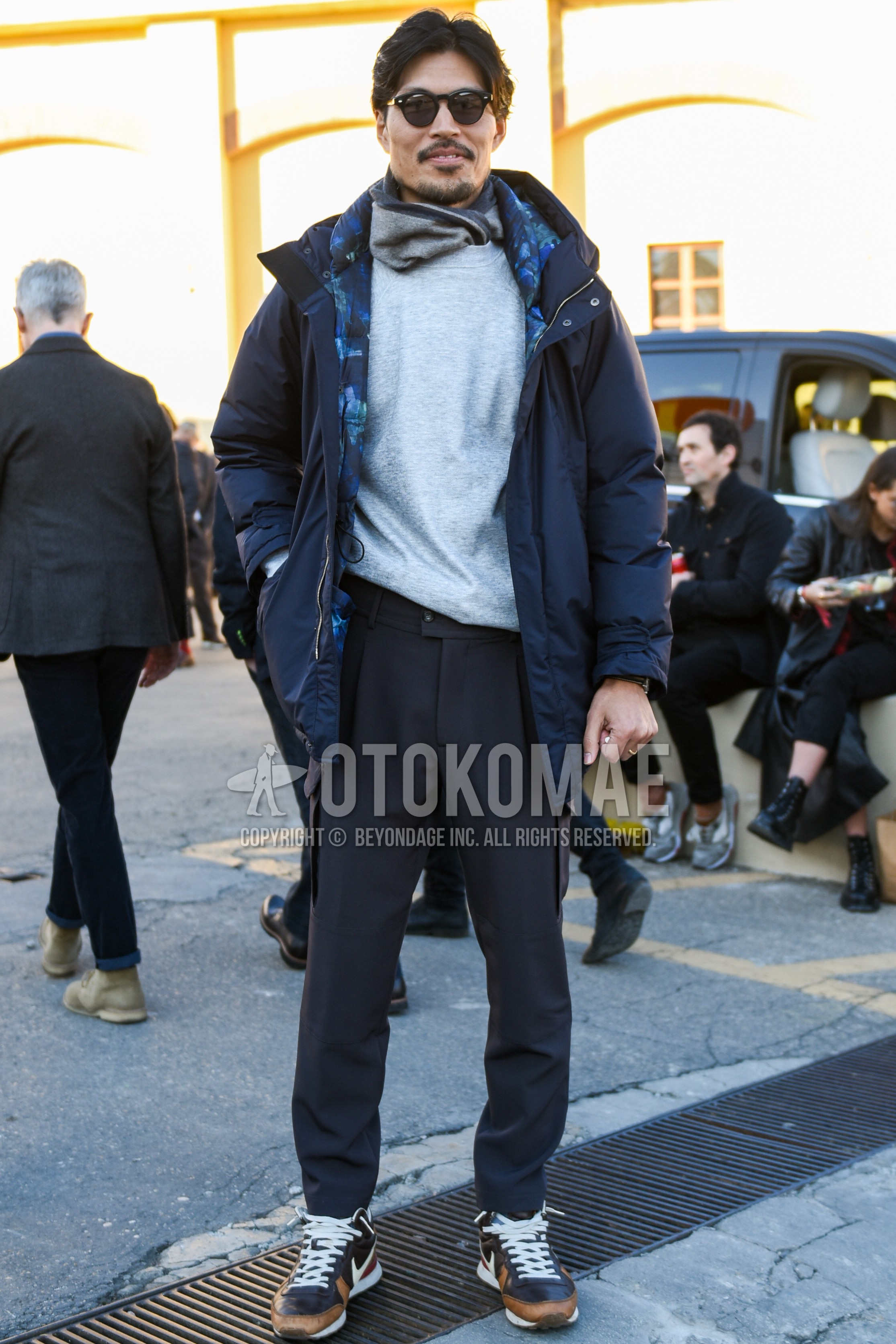 Men's winter outfit with black plain sunglasses, gray plain scarf, dark gray plain hooded coat, gray plain sweatshirt, gray plain slacks, gray plain cargo pants, brown navy low-cut sneakers.
