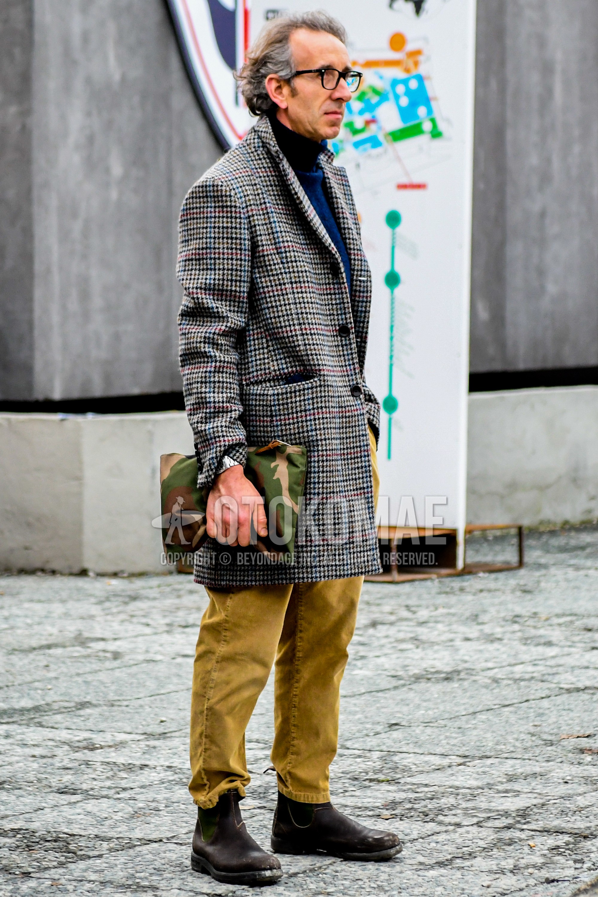 Men's winter outfit with plain glasses, gray check chester coat, blue plain turtleneck knit, beige plain chinos, brown side-gore boots, multi-color camouflage clutch bag/second bag/drawstring bag.