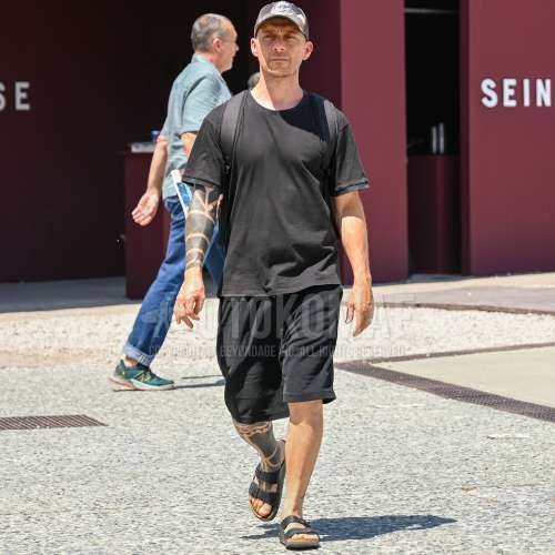 マルチカラー迷彩のベースボールキャップ、黒無地のTシャツ、黒無地のショートパンツ、ビルケンシュトック　アリゾナの黒レザーサンダル、黒無地のバックパックを合わせた夏春のメンズコーデ・着こなし。