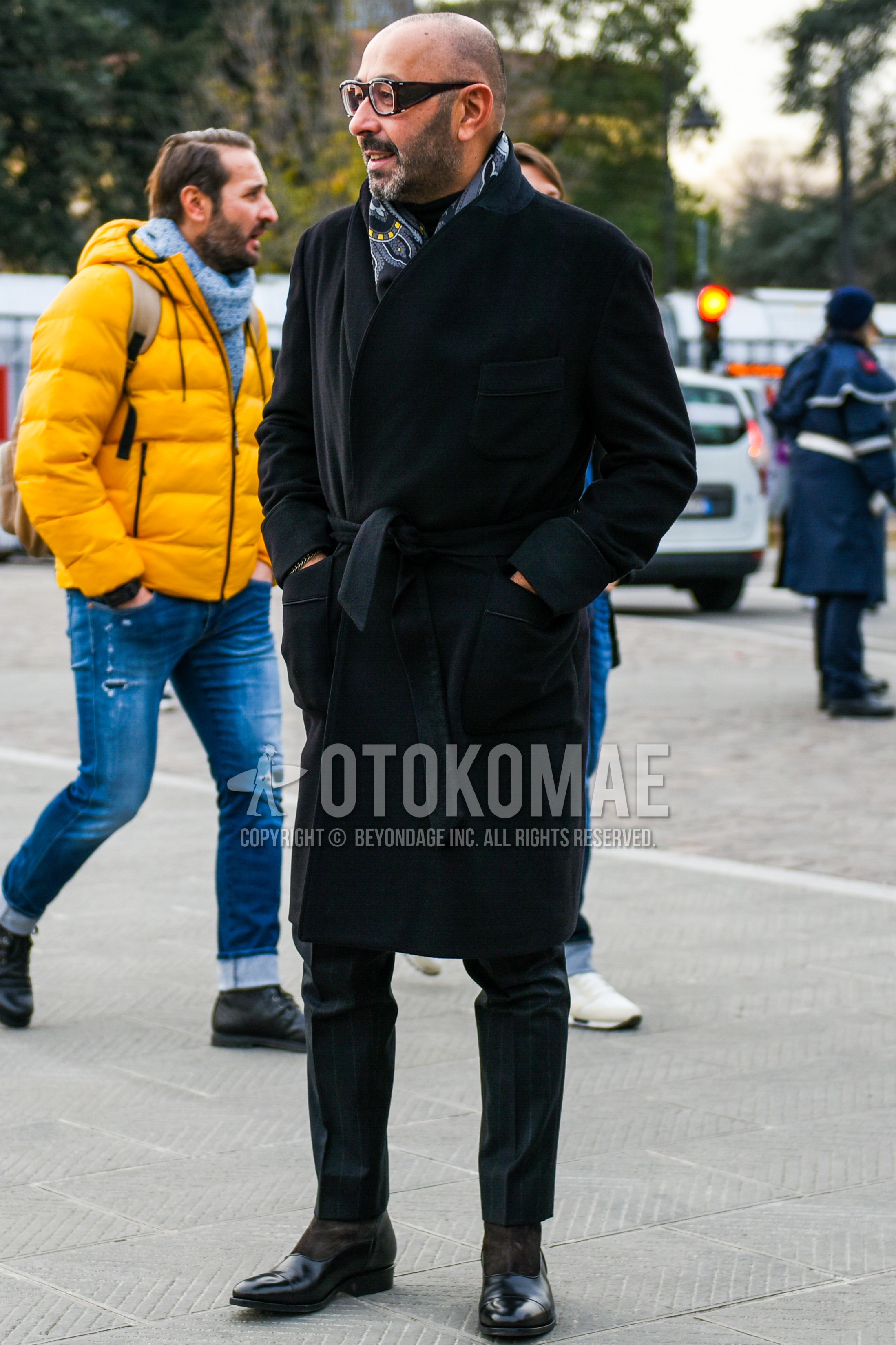 Men's autumn winter outfit with black plain glasses, gray paisley scarf, black plain belted coat, black plain slacks, black  boots.