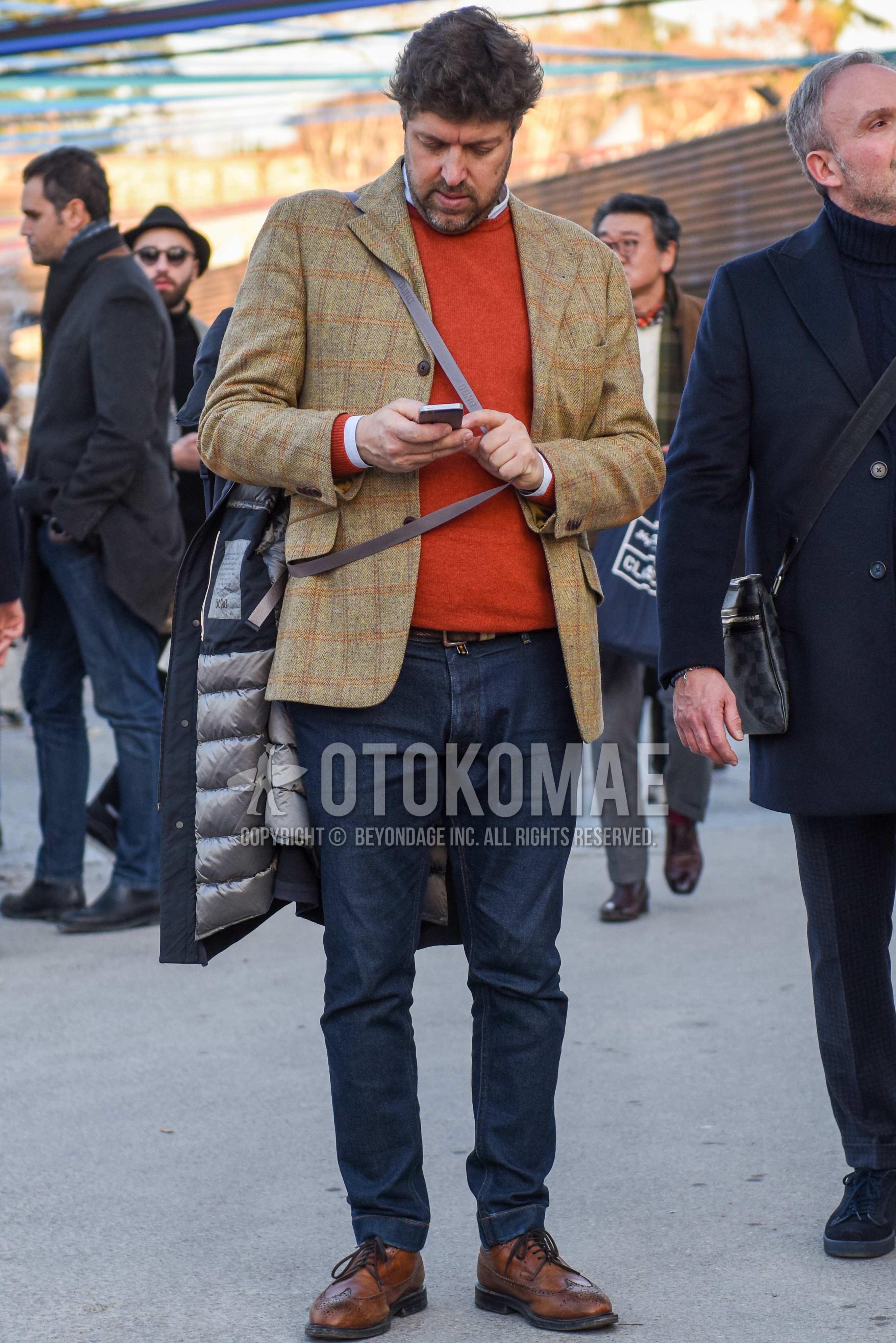 Men's spring autumn outfit with beige check tailored jacket, orange plain sweater, white plain shirt, brown plain leather belt, navy plain denim/jeans, brown wing-tip shoes leather shoes.
