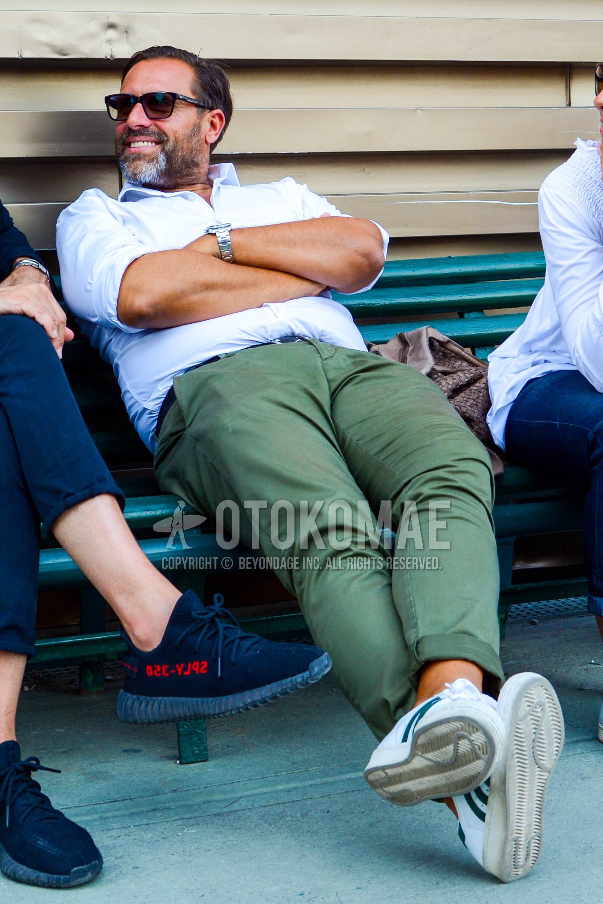 Men's spring summer outfit with plain sunglasses, white plain shirt, olive green plain chinos, white low-cut sneakers.