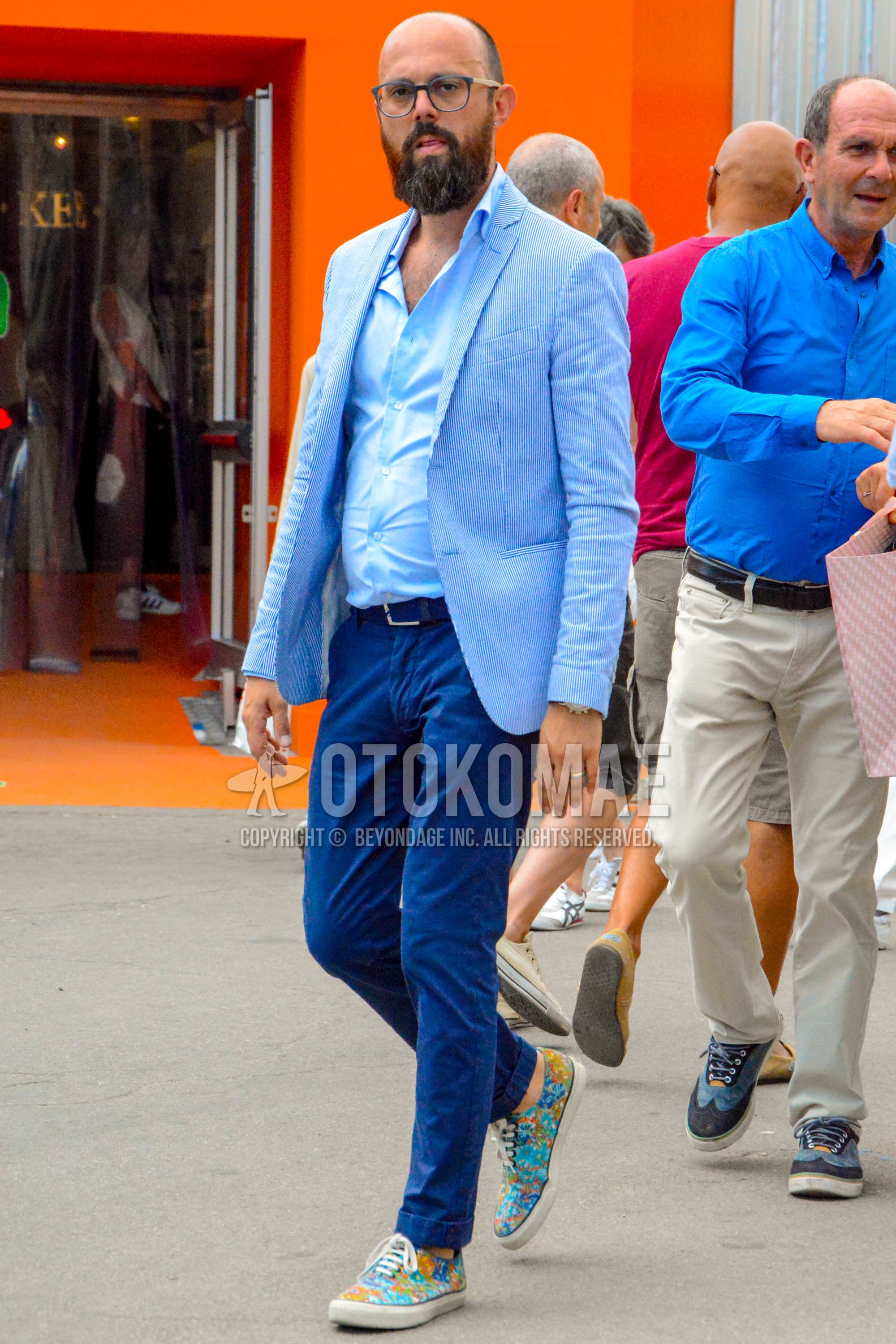 Men's spring summer autumn outfit with gray plain glasses, light blue stripes tailored jacket, light blue plain shirt, blue plain leather belt, blue plain chinos, multi-color low-cut sneakers.