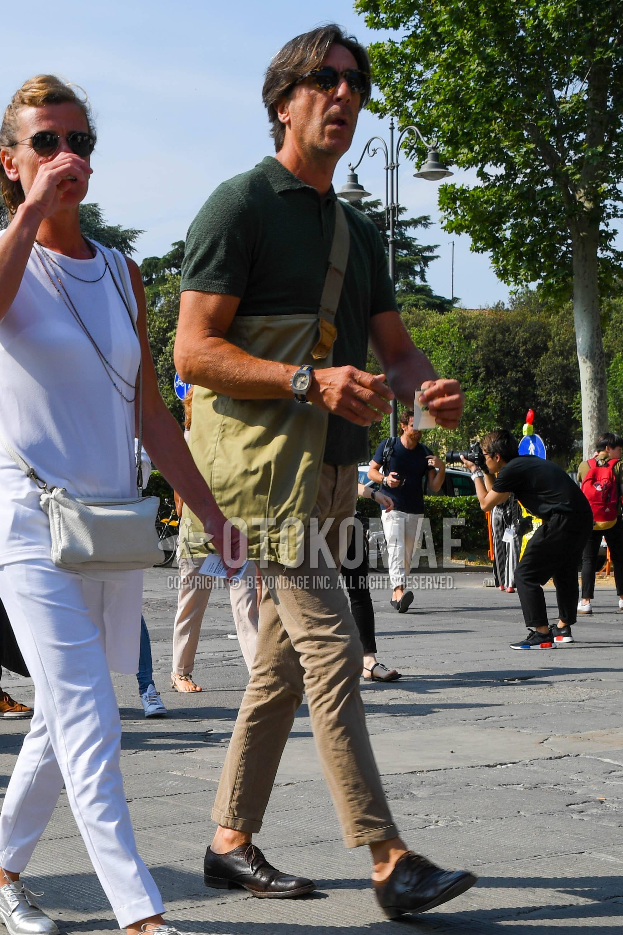 Men's summer outfit with plain sunglasses, olive green plain polo shirt, beige plain chinos, plain ankle pants, brown plain toe leather shoes, beige plain shoulder bag.