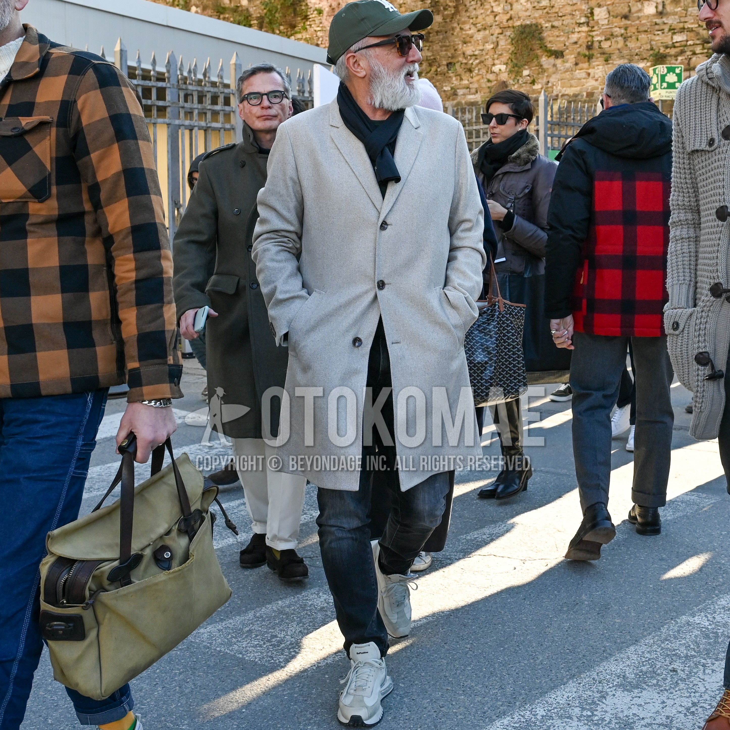 Men's autumn winter outfit with olive green one point baseball cap, navy plain scarf, beige plain chester coat, black plain denim/jeans, white low-cut sneakers.