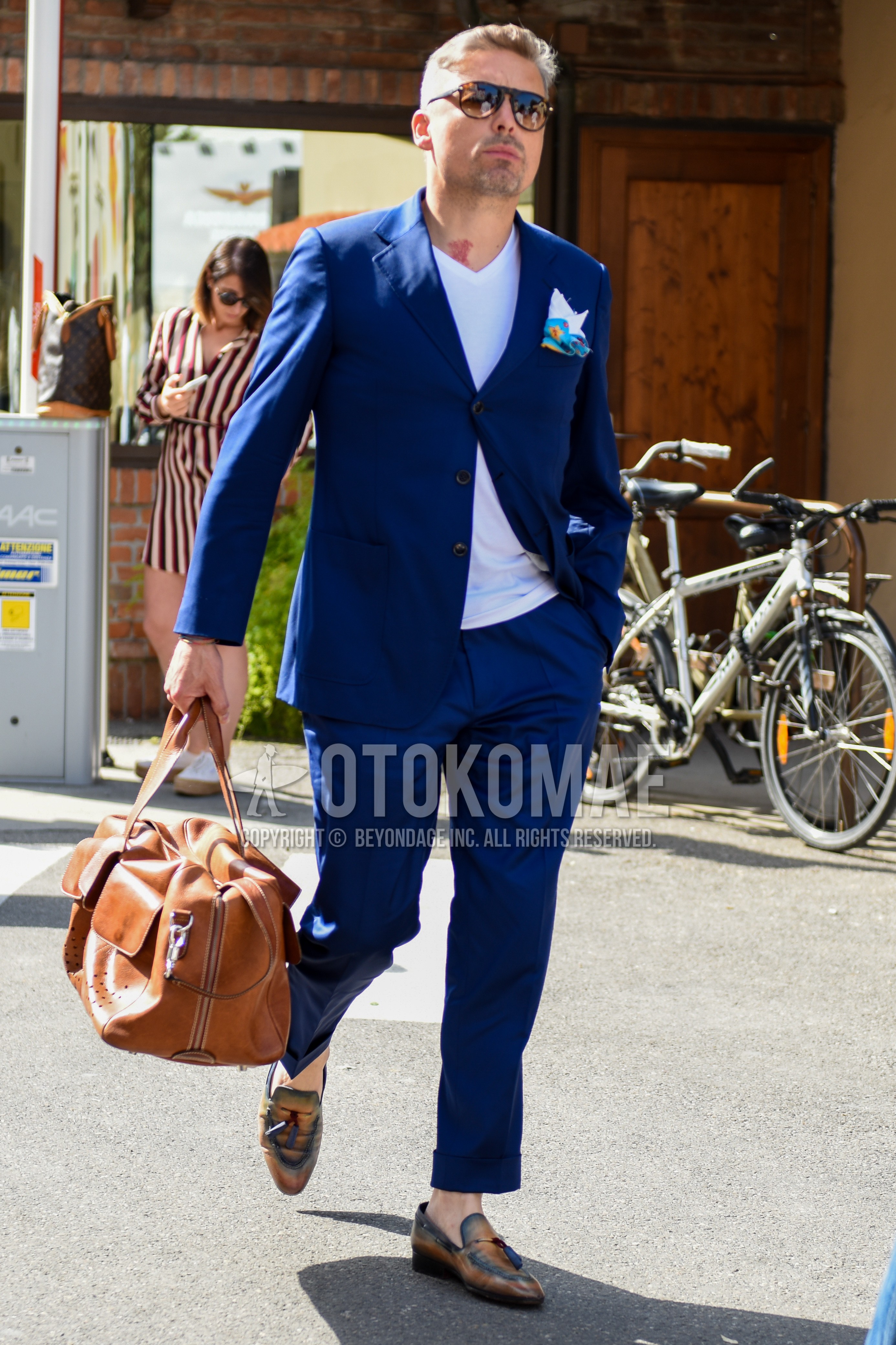 Men's spring summer outfit with brown tortoiseshell sunglasses, white plain t-shirt, beige tassel loafers leather shoes, brown plain boston bag, navy plain suit.
