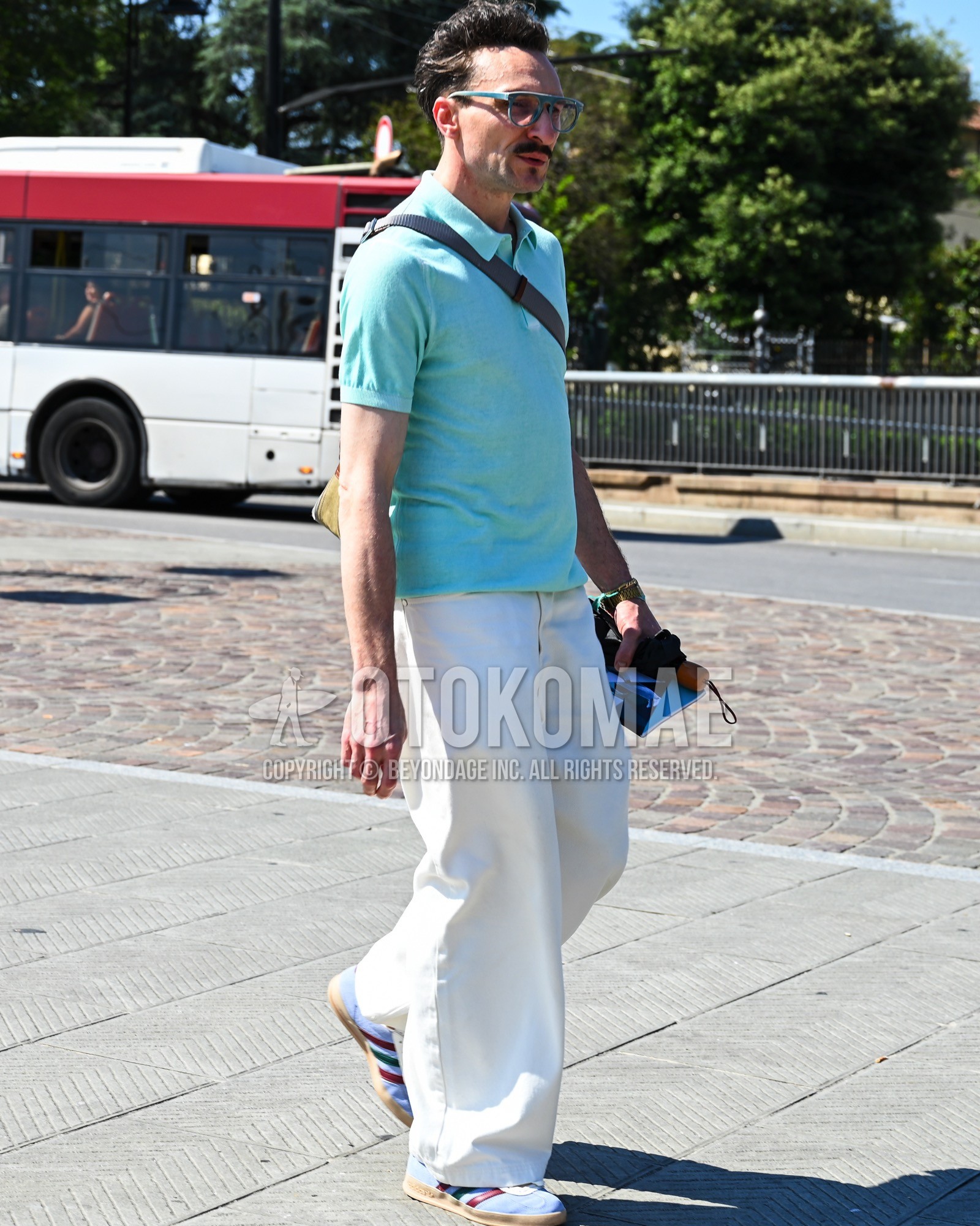 Men's spring summer outfit with clear plain sunglasses, light blue plain polo shirt, white plain wide pants, light blue low-cut sneakers, black plain shoulder bag.