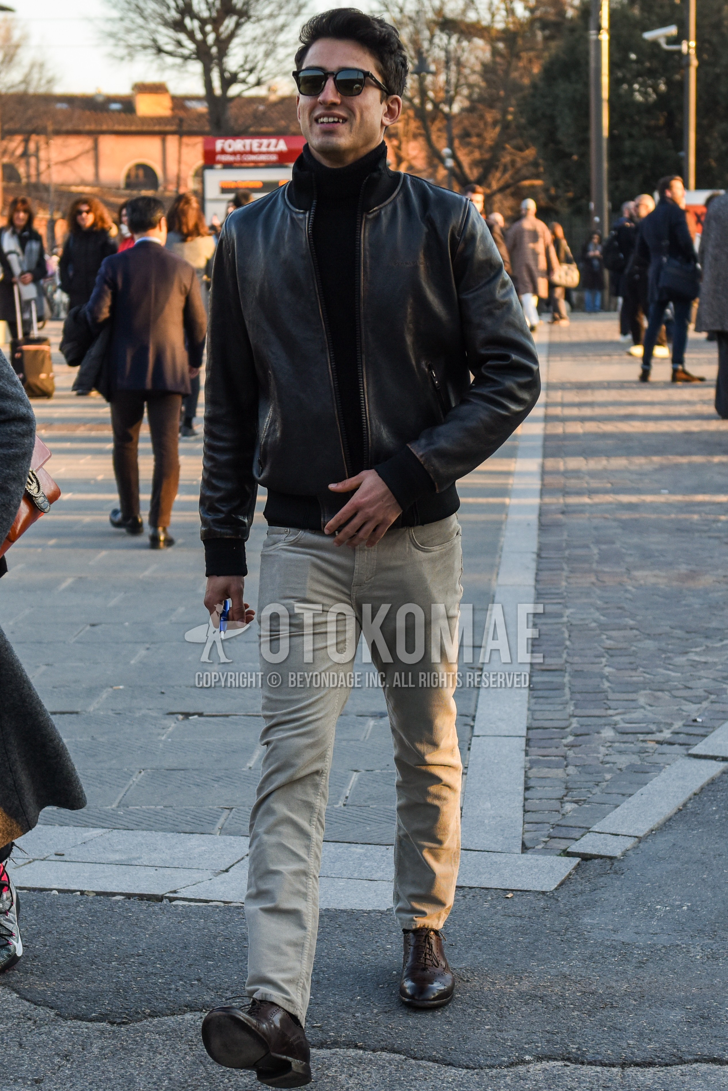 Men's autumn winter outfit with black plain sunglasses, black plain leather jacket, black plain turtleneck knit, beige plain chinos, brown brogue shoes leather shoes.